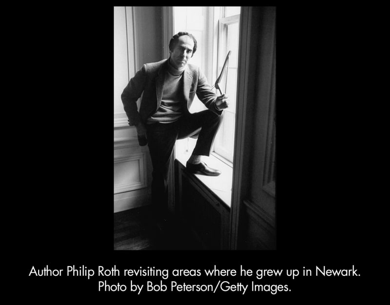 Author Philip Roth revisiting areas where he grew up in Newark. Photo by Bob Peterson/Getty Images.  A light-skinned, dark-haired man with a receding hairline stands with one foot on a window.