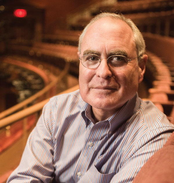 Todd Haimes in a theatre seat in the empty American Airlines Theatre in the mezzanine. He is facing the camera and smiling.