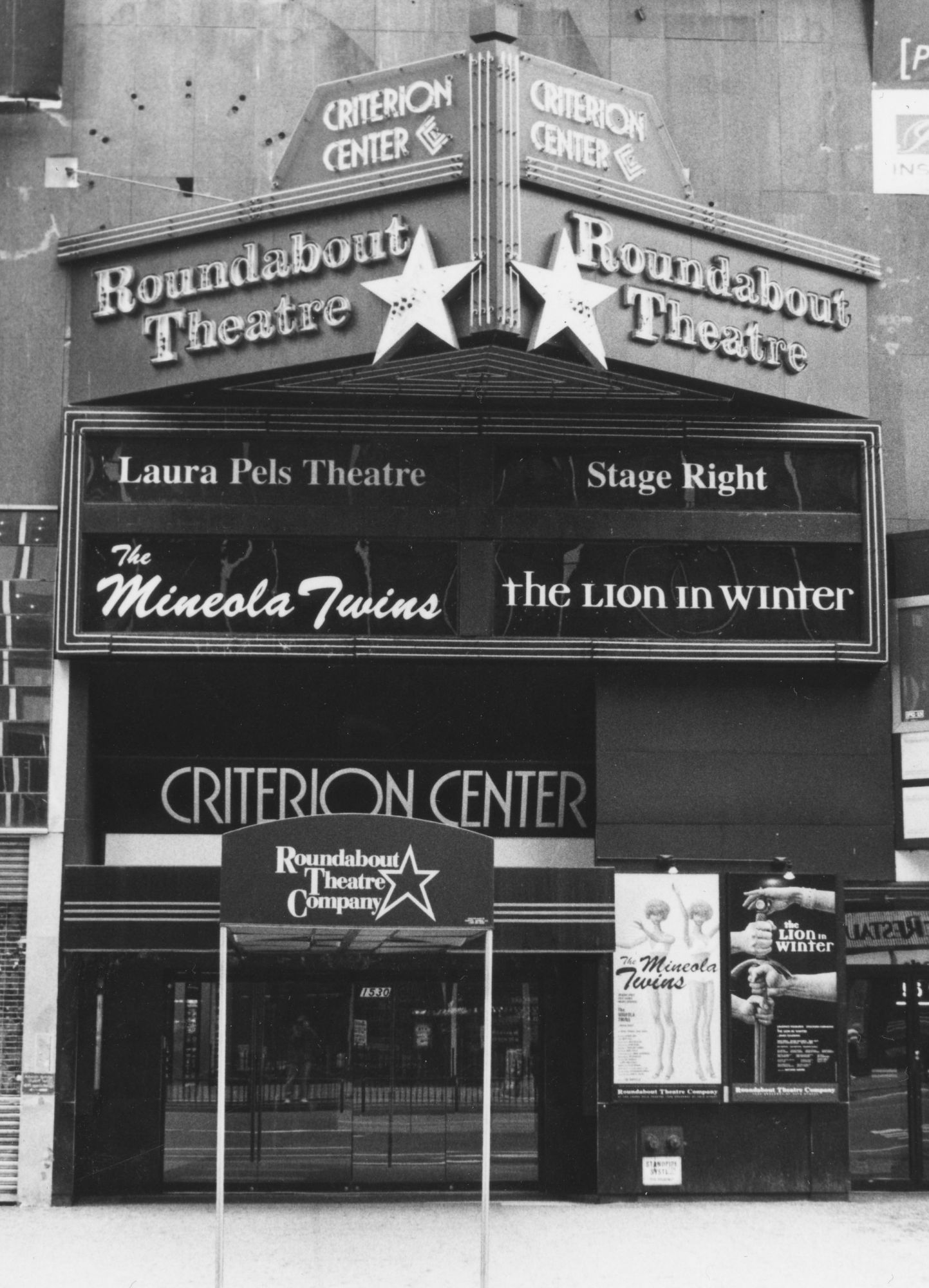 Black and white photo of the Criterion Center. The marquee says Roundabout Theatre with a big star. Below it are marquees for shows The Mineola Twins and The Lion in Winter