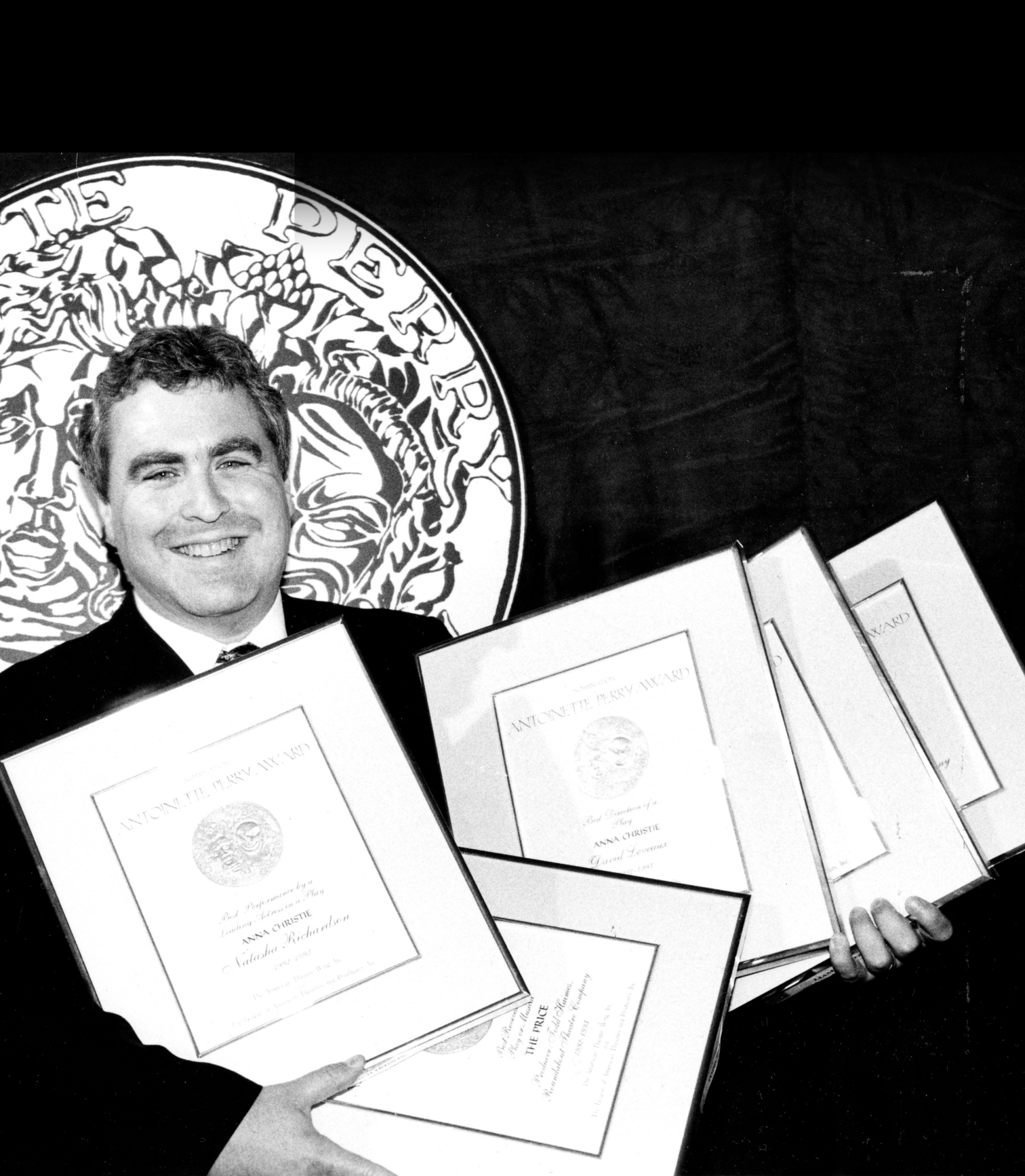 Black and white photo of Todd Haimes holding 5 frames containing Tony Awards nominations.