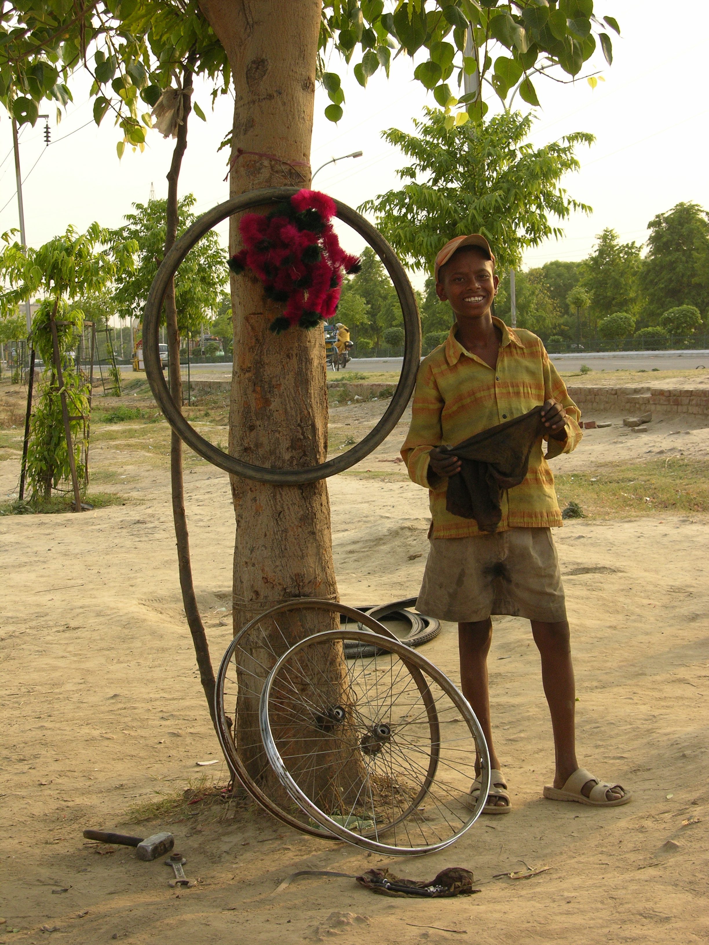 A peepul tree is really the people’s tree. Shop or temple, it showers its blessings. The colourful wheel decor for cycles draws the eye to the shop. Despite a hot summer day, a smile is readily offered to a camera.
 
