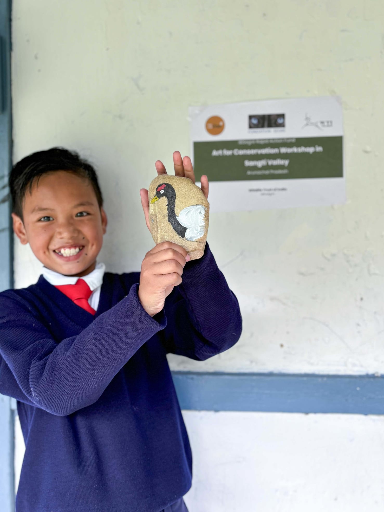 A boy holds up artwork with a black-necked crane. 