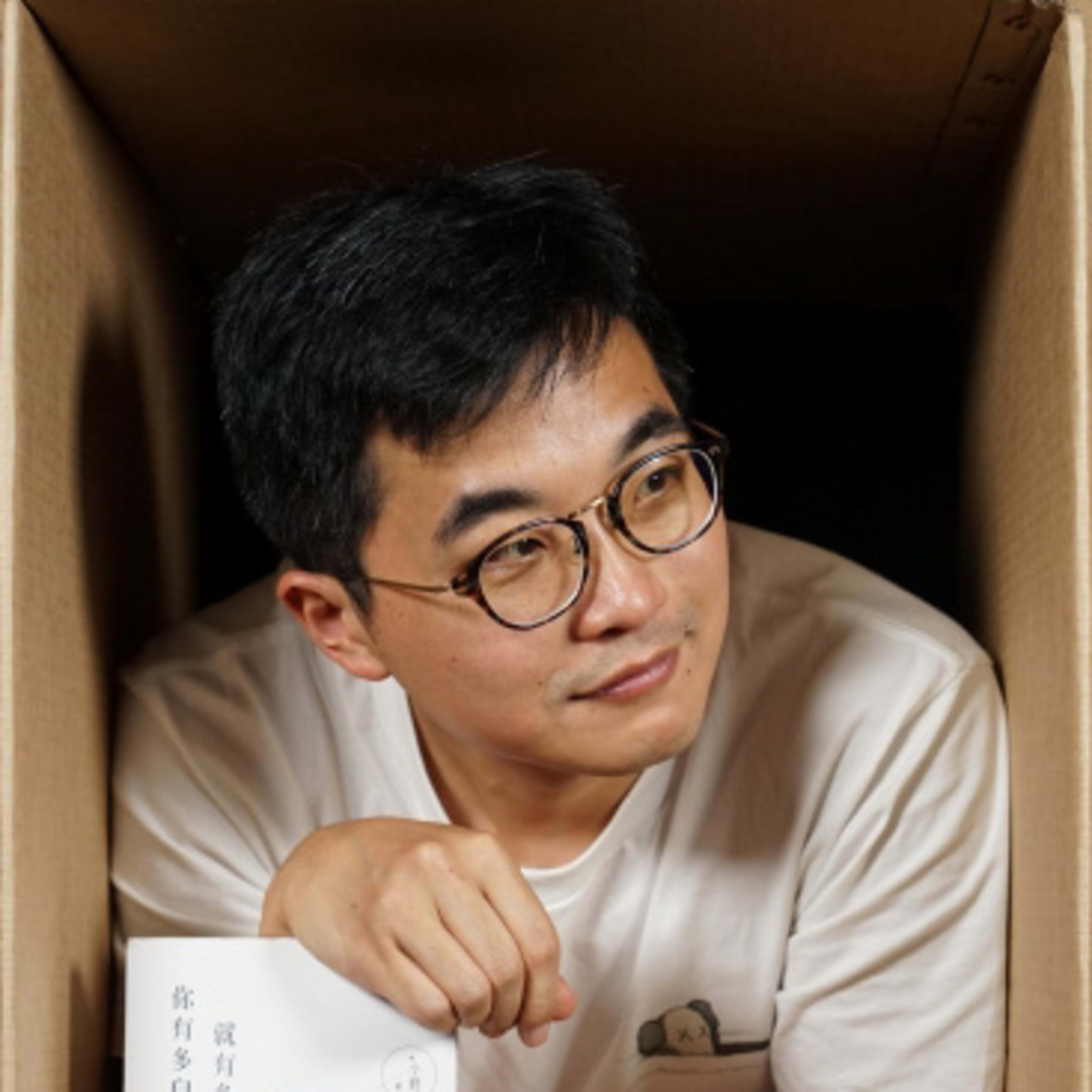 天台製作（Rooftop Productions）演員陳冠宏的劇照。照片中他身處一個紙箱內，雙手撐在箱緣，手持書籍《就有多自由，你就有多自律》。溫暖的攝影棚燈光映照著他若有所思的神情，呈現出香港當代劇場獨特的實驗感與親密氛圍。陳冠宏。