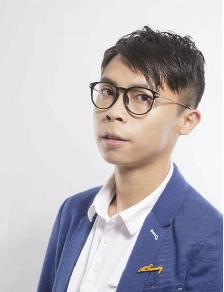 香港劇場演員趙展禧的個人宣傳照，於純淨的背景下拍攝。他身穿深藍色西裝外套內搭白襯衫，並佩戴黑色膠框眼鏡，展現出「天台製作」當代劇場表演者的專業形象。這張人像照突顯了他作為香港獨立劇場界重要演員的獨特氣質。