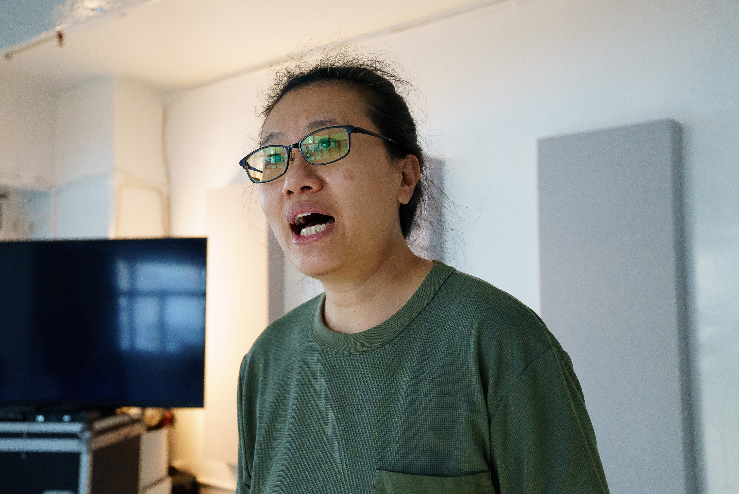 演員李婉晶（Michelle Li）於天台製作（Rooftop Productions）當代劇場作品《卡啦OK》排練期間的近照。她戴著眼鏡，身穿綠色上衣，在排練室中全神貫注地進行情感投入的排演。『《卡啦OK》排練』