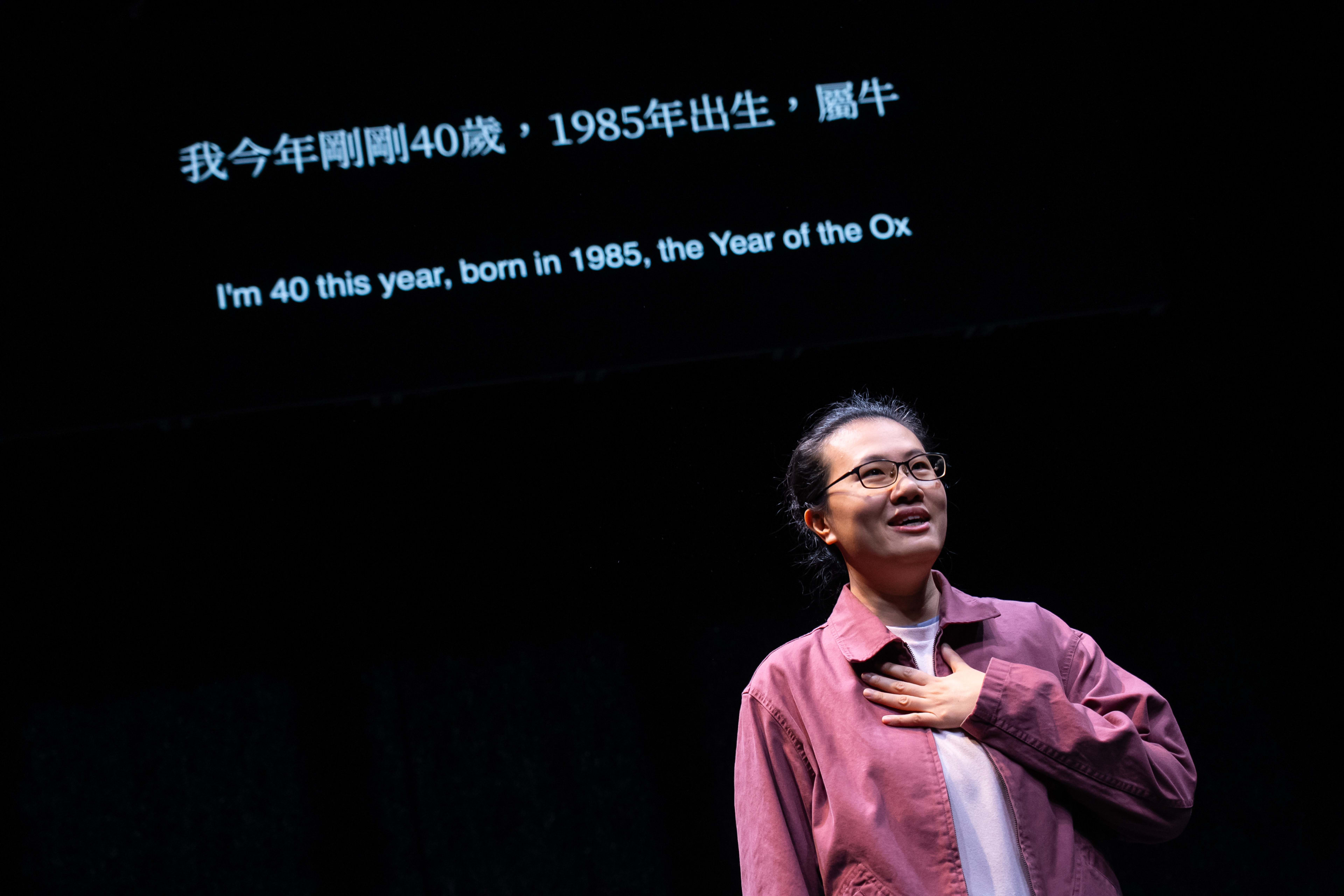 在天台製作（Rooftop Productions）的當代劇場作品《卡啦OK》中，演員李婉晶站在昏暗的舞臺聚光燈下，身穿紫紅色休閒外套，內搭白色上衣。她神情溫柔而沉思，一隻手輕撫心口，仰望觀眾席。背景的投影屏幕上顯示著：「我今年剛剛40歲，1985年出生，屬牛」。李婉晶隨即演繹了這句台詞：「我今年剛剛40歲，1985年出生，屬牛」。