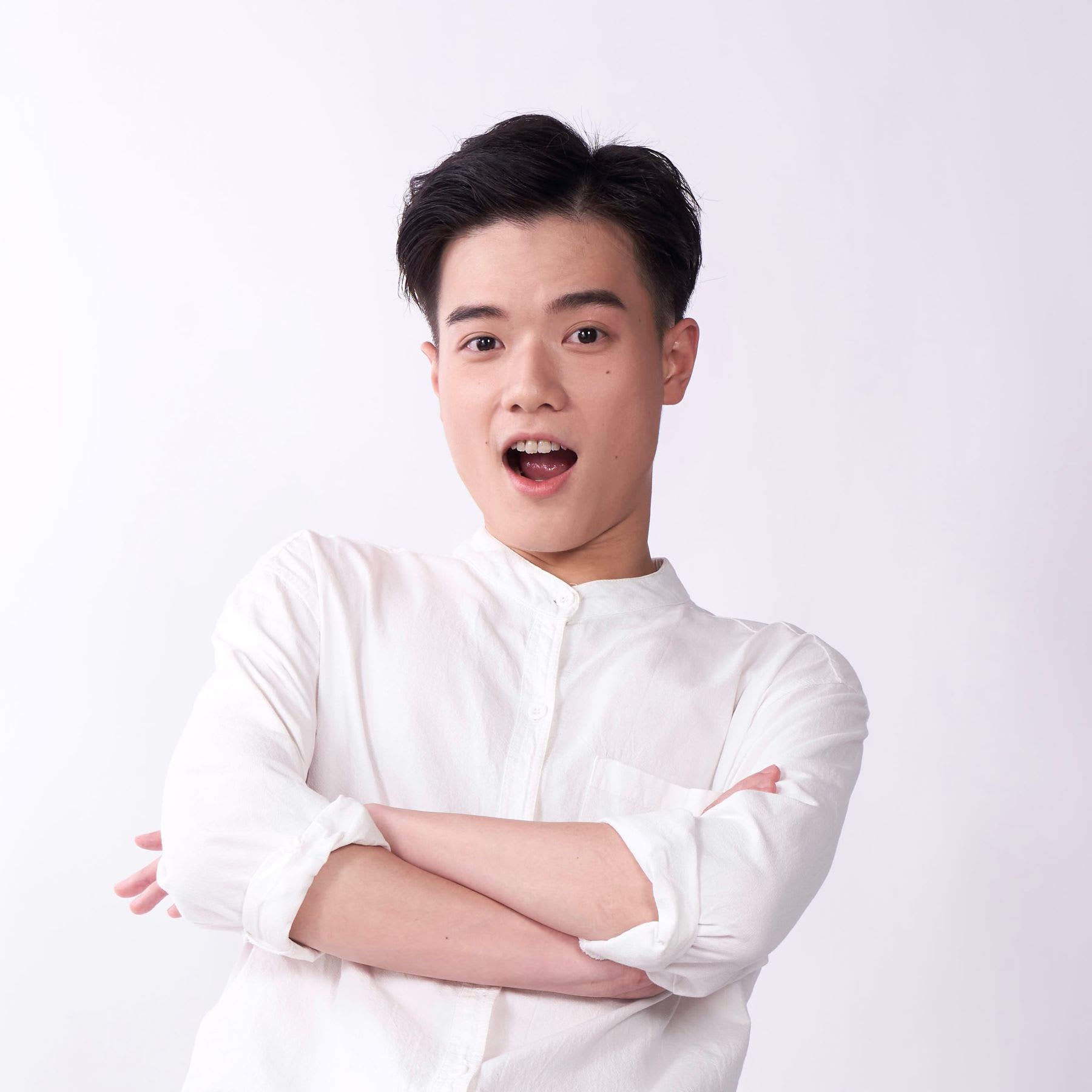香港演員羅文澤的半身宣傳照，以簡約純淨的背景為襯。照片中的他雙臂交叉胸前，穿著一件捲起衣袖的白色休閒襯衫。他神情生動，雙眼炯炯有神，開口微笑的模樣展現出香港當代劇場表演中常見的活力與熱情。宣傳照。