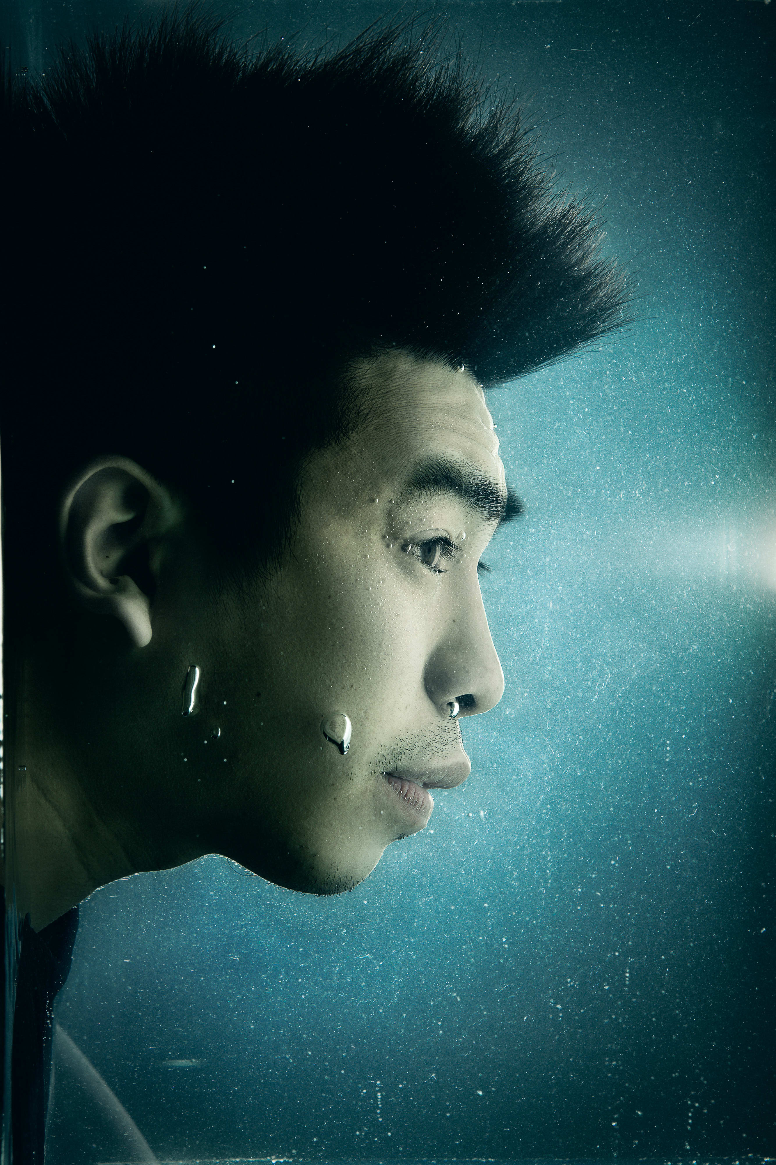 演員吳紹熙（Larry Ng）在水底下的戲劇性側面特寫，頭髮在幽暗深邃的藍色背景中向上漂浮，形成凌厲的剪影。細小的氣泡依附在他臉頰上，隨水流漂浮，營造出天台製作（Rooftop Productions）標誌性的前衛劇場氛圍。這張當代香港劇場作品《消失的海岸線》宣傳照，捕捉了該劇深刻的張力與內省情感。《消失的海岸線》