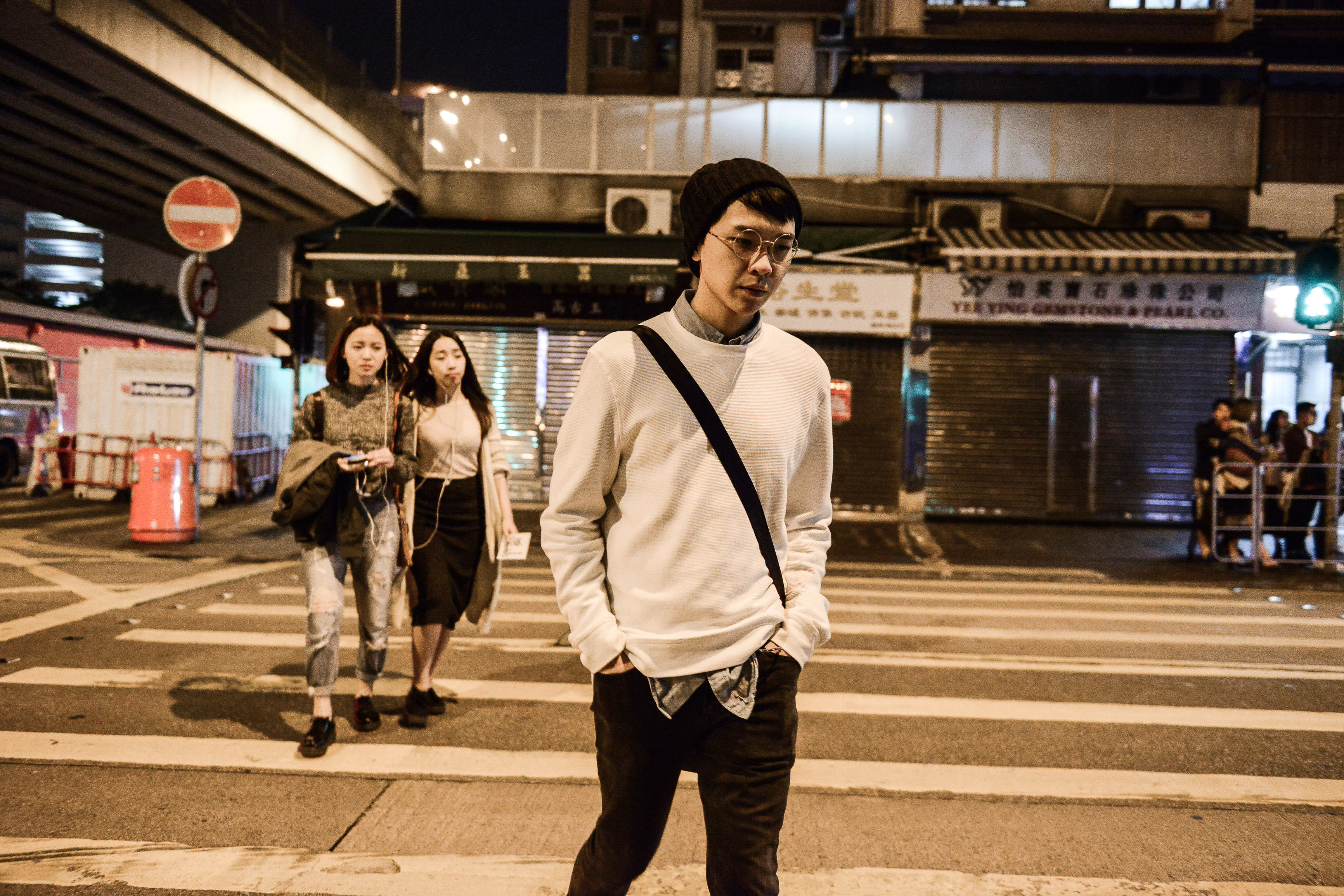 在天台製作的當代劇場作品《消失的海岸線》中，演員吳景隆於夜間穿過城市斑馬線。他身穿白色衛衣並配戴黑色冷帽與眼鏡，背著斜挎包，後方還有兩名演員跟隨。燈光營造出充滿電影感的憂鬱氛圍，體現了天台製作對在地身份認同的深度探索。《消失的海岸線》