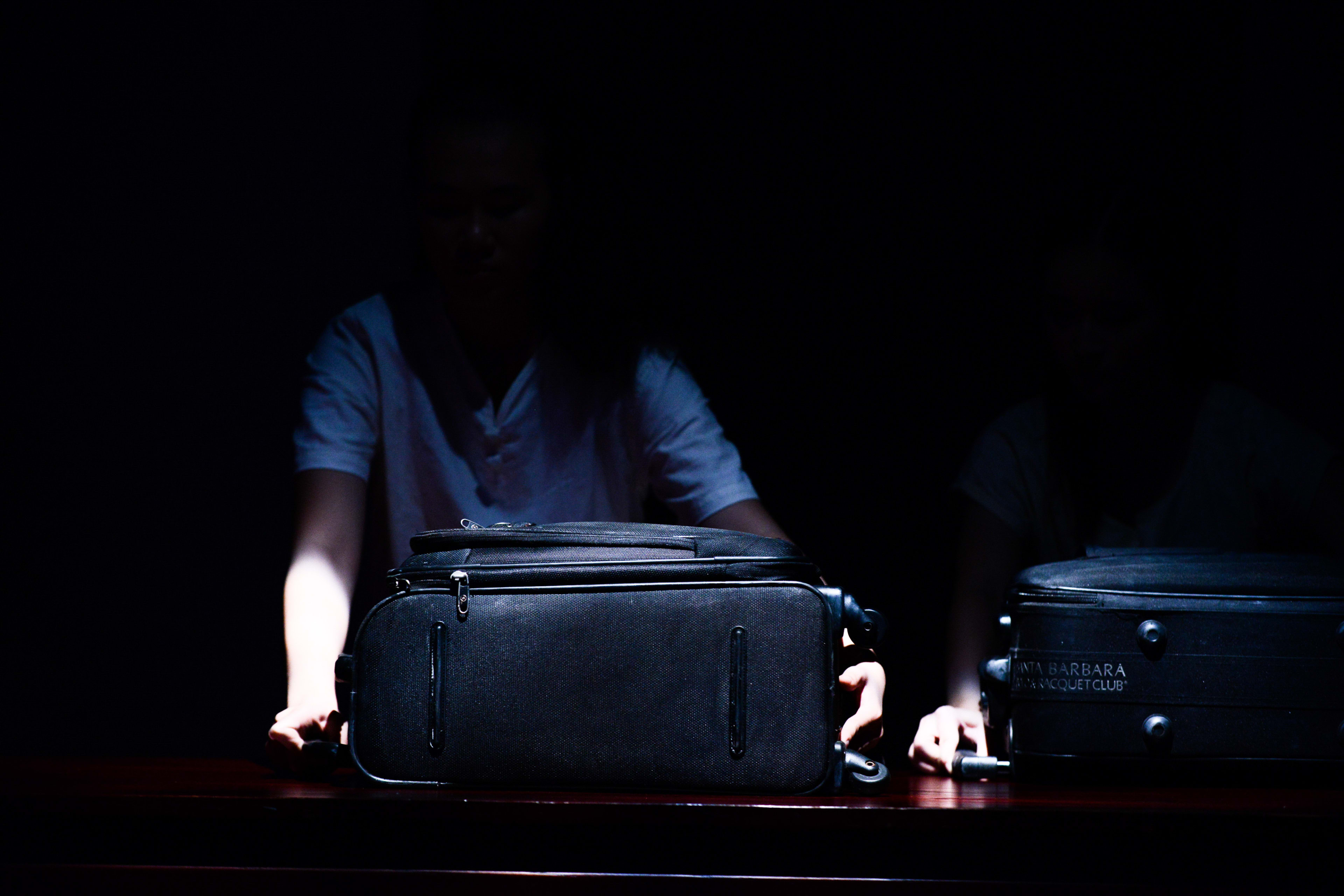 在這張天台製作（Rooftop Productions）當代劇場作品《牛奶與蜜糖》的排練照中，兩位演員身處陰影之中，僅被一束聚光燈照亮。他們站在深色木桌後，雙手輕撫著兩個黑色行李箱，為這部香港舞台劇增添了一份關於旅程、離別或轉變的戲劇張力。《牛奶與蜜糖》