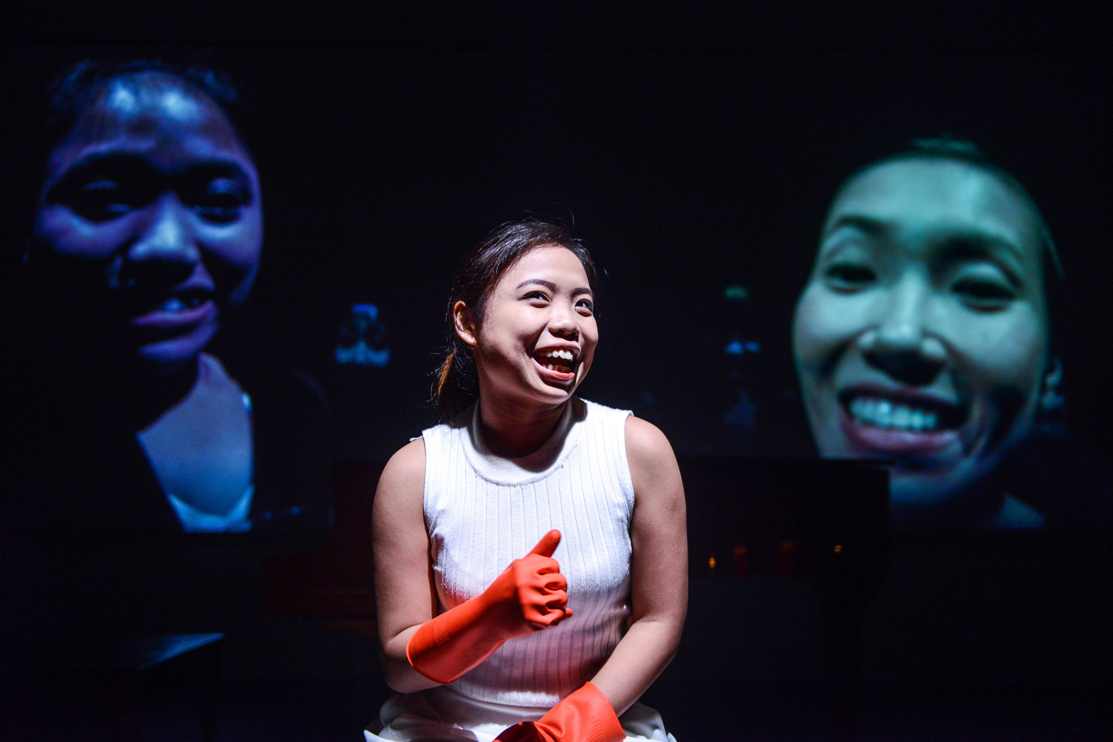 在天台製作的當代劇場作品《不是女僕》中，演員梁皓貽（Isabella Leung）身穿白色上衣，戴著橙色橡膠手套，神情愉悅地做出豎起拇指的手勢。舞台背景黑暗，兩旁投射出巨大的臉部影像，營造出香港實驗劇場特有的多層次視覺效果。演出中她說道：「我不知道...可能我喜歡小孩子？」