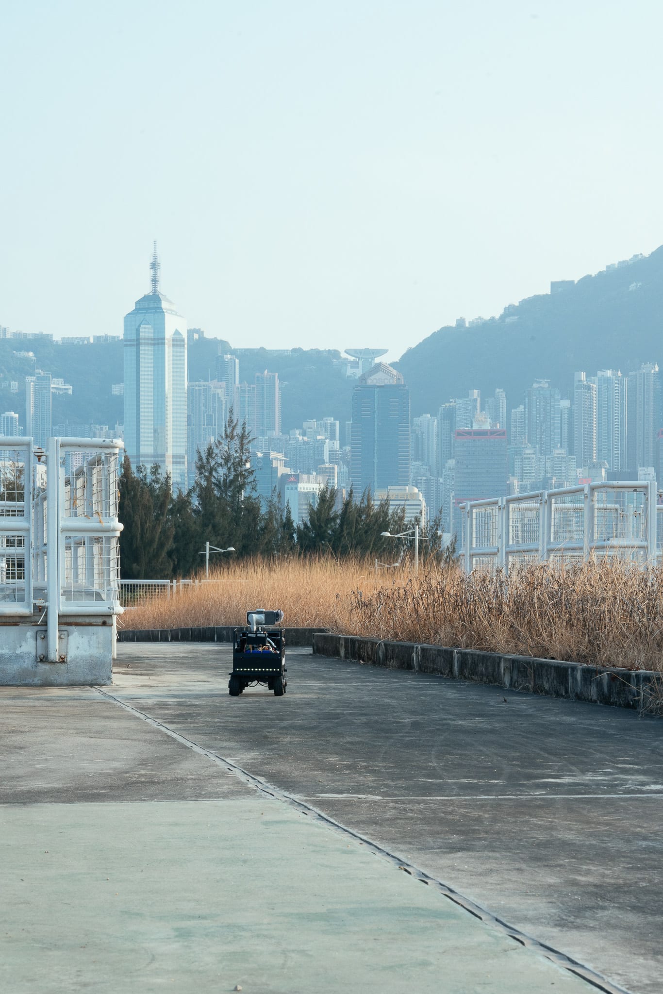 一台小型自動化攝錄機器人佇立在荒涼的水泥天台上，遠眺香港朦朧且密集的城市天際線，背景映襯著群山。此極簡的舞台佈置手法，呼應了天台製作（Rooftop Productions）當代劇場作品《遙距在場》中關於距離與數位媒介的主題。西九項目辦公室天台。