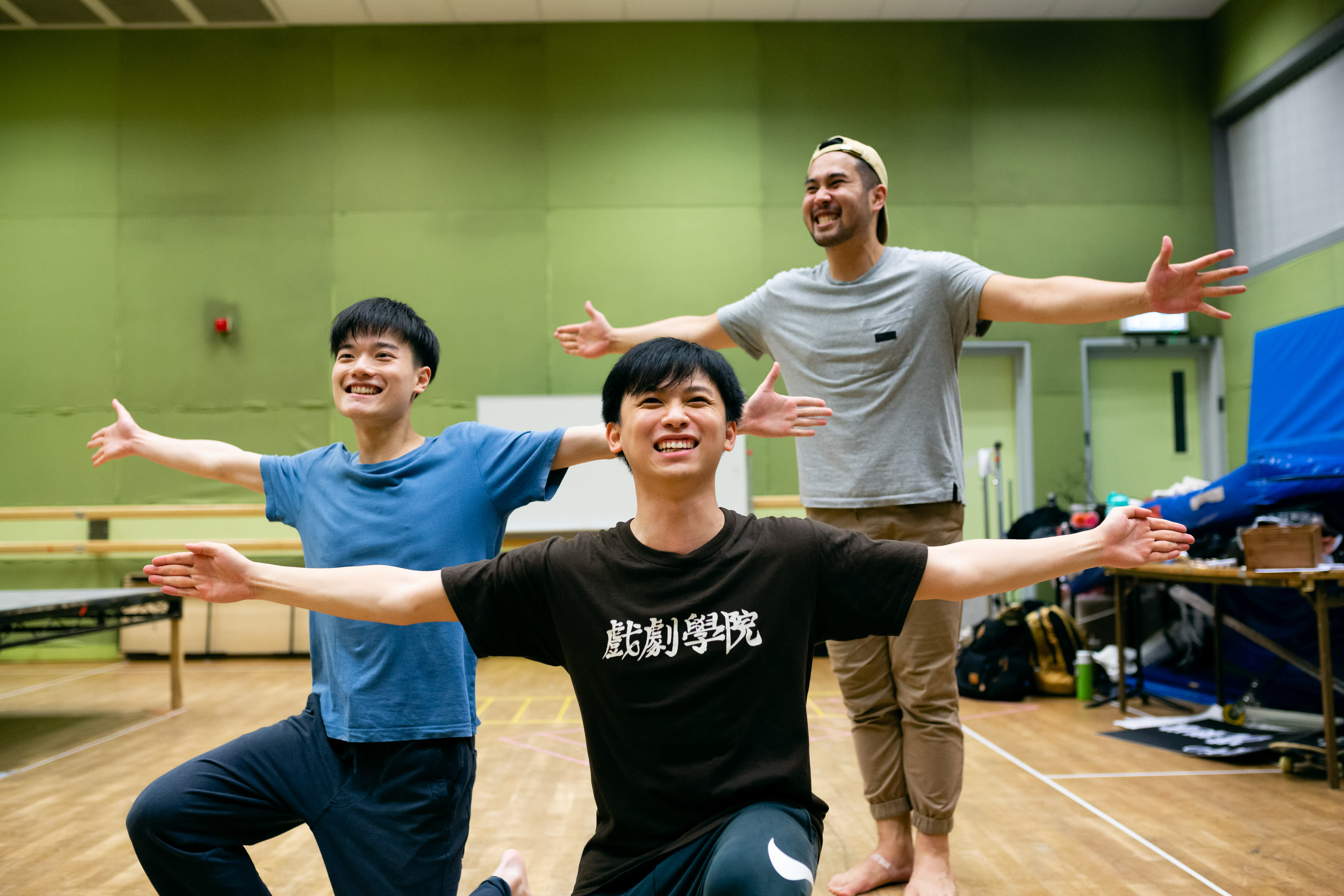 這是一場由香港當代劇團「天台製作」為舞台劇《天真與世故之歌》進行的排練。演員趙汝陽、羅文澤及莫珏邦在排練室中，以雙臂張開的姿態呈現出充滿張力的肢體動作，神情展現出作品中探討的純真與世故。透過富有感染力的表演，他們正演繹該劇的核心情感。 《天真與世故之歌》排練。