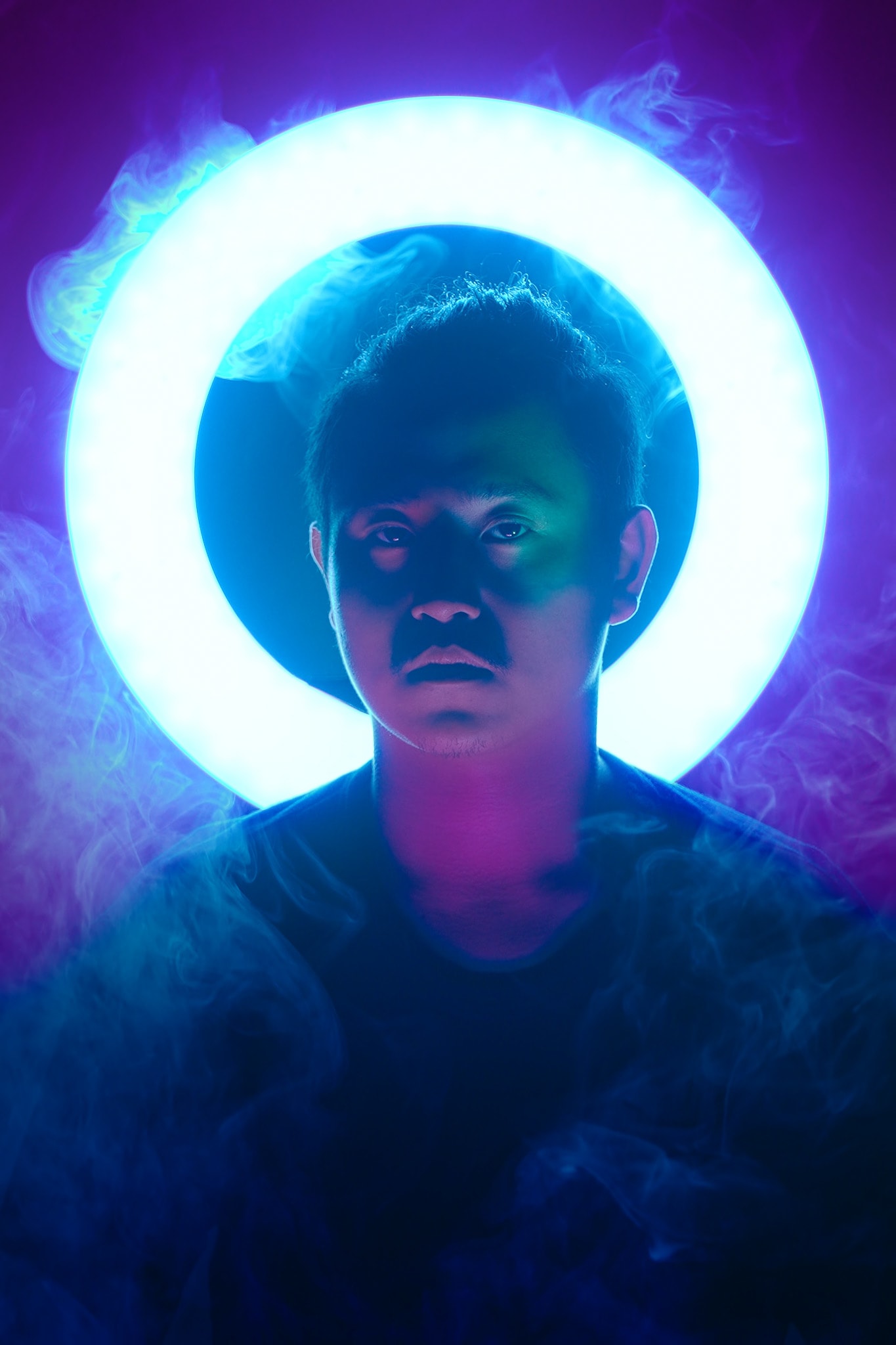 天台製作（Rooftop Productions）當代劇場作品《天真與世故之歌》的戲劇性宣傳照。樂手宋國通處於畫面中央，頭部後方設有一圈明亮的藍色光環，為其臉部投下深邃的陰影。周圍環繞著藍紫色的舞臺煙霧，營造出香港當代劇場獨有的冷峻與沉思氛圍。宋國通，《天真與世故之歌》西九文化區。