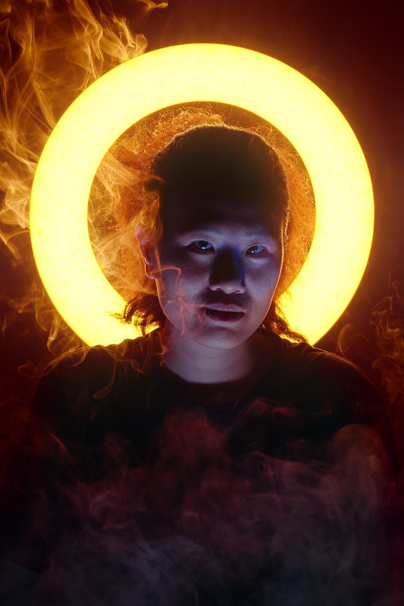 這是一張為天台製作（Rooftop Productions）當代劇場作品《天真與世故之歌》拍攝的極具戲劇張力宣傳照，由演員李婉晶（Michelle Li）出鏡。畫面中，她背後有一個明亮的黃色圓形光環，營造出宛如聖光的視覺效果。煙霧繚繞在她周圍，與光影交織，營造出充滿內省與藝術深度的氛圍，展現了西九文化區演出的獨特質感。《天真與世故之歌》西九文化區