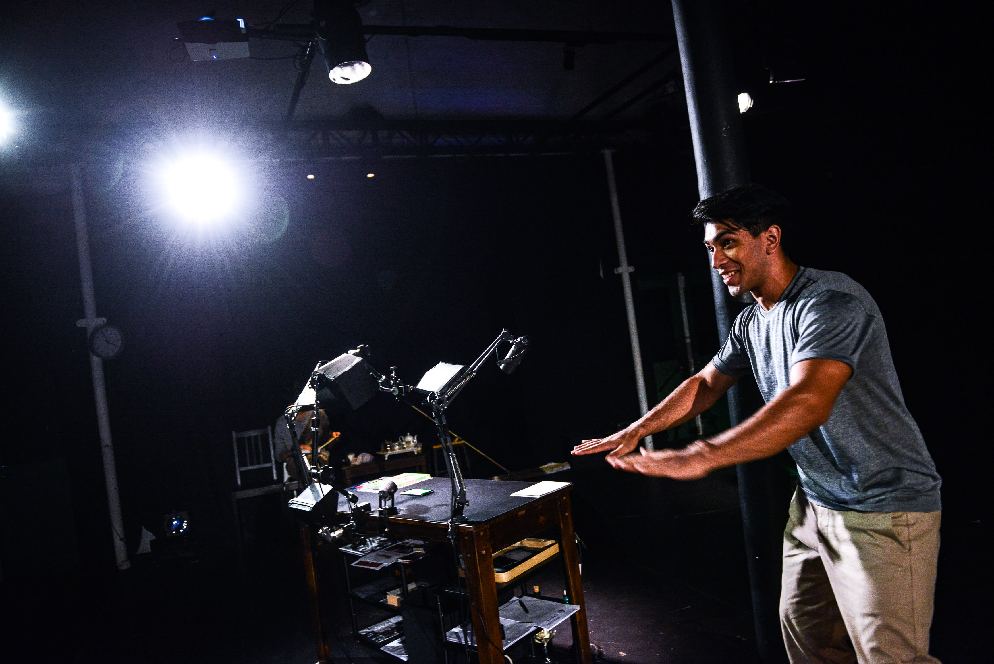在天台製作 (Rooftop Productions) 的當代劇場作品《山下的證詞》(Testimony) 中，演員巫加沙 (Mohammad Kashif Ali) 站在燈光幽暗的舞台上，身體轉向一張佈滿演出道具與器材的中央桌子。他在頭頂強烈的聚光燈照射下，以充滿張力的手勢進行演繹，完美呈現了這場香港當代戲劇的深刻情感與敘事氛圍。《山下的證詞》