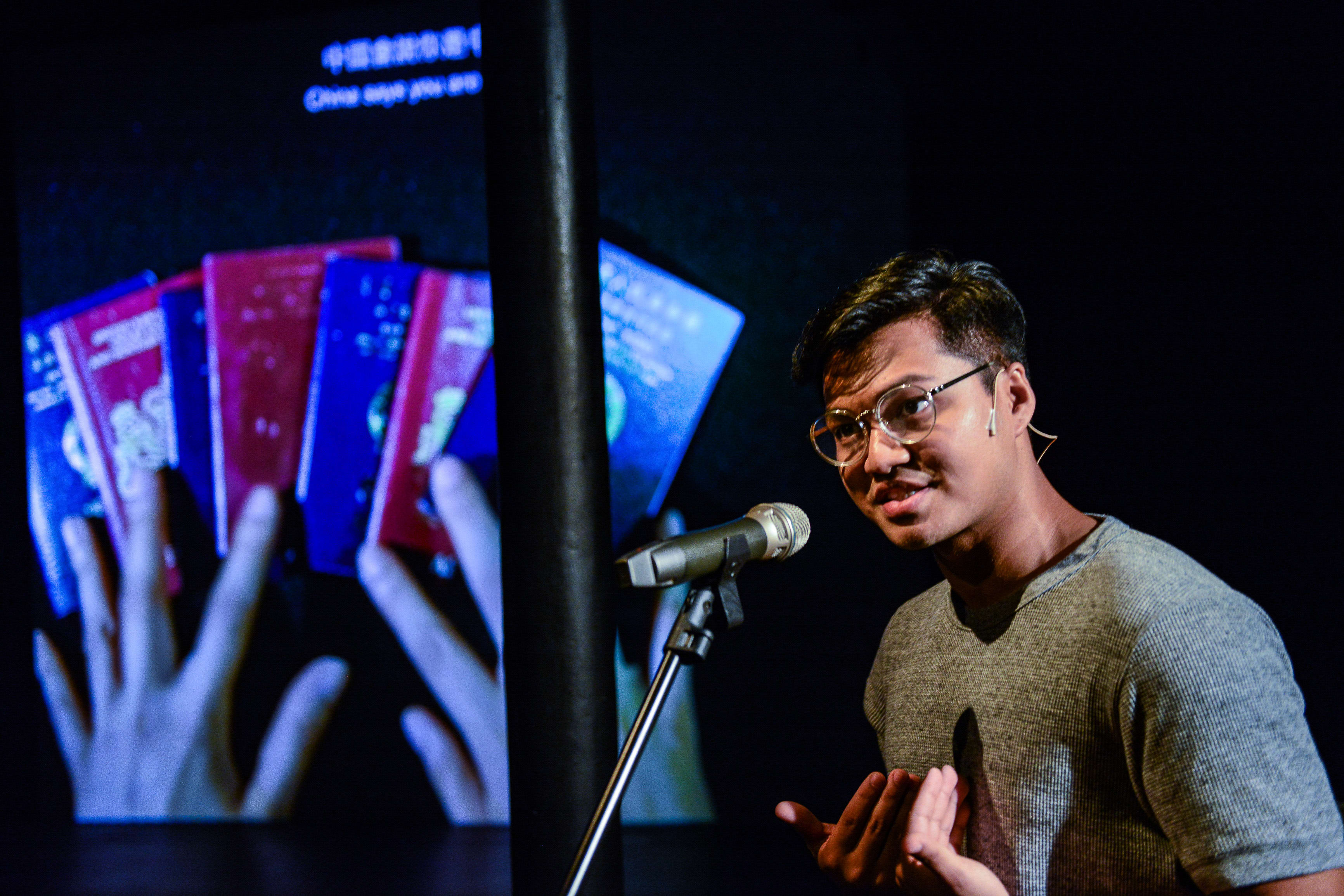 Basnet Tusar 於天台製作 (Rooftop Productions) 當代劇場作品《山下的證詞》(Testimony) 中進行感人演出。在戲劇性的舞台燈光下，他手持麥克風，對著背景中投影出雙手持有護照的影像，訴說著香港人的身份掙扎。他隨即說道：「所以，基本上在1997年後，我們並沒有國家，成為沒有家的人。」