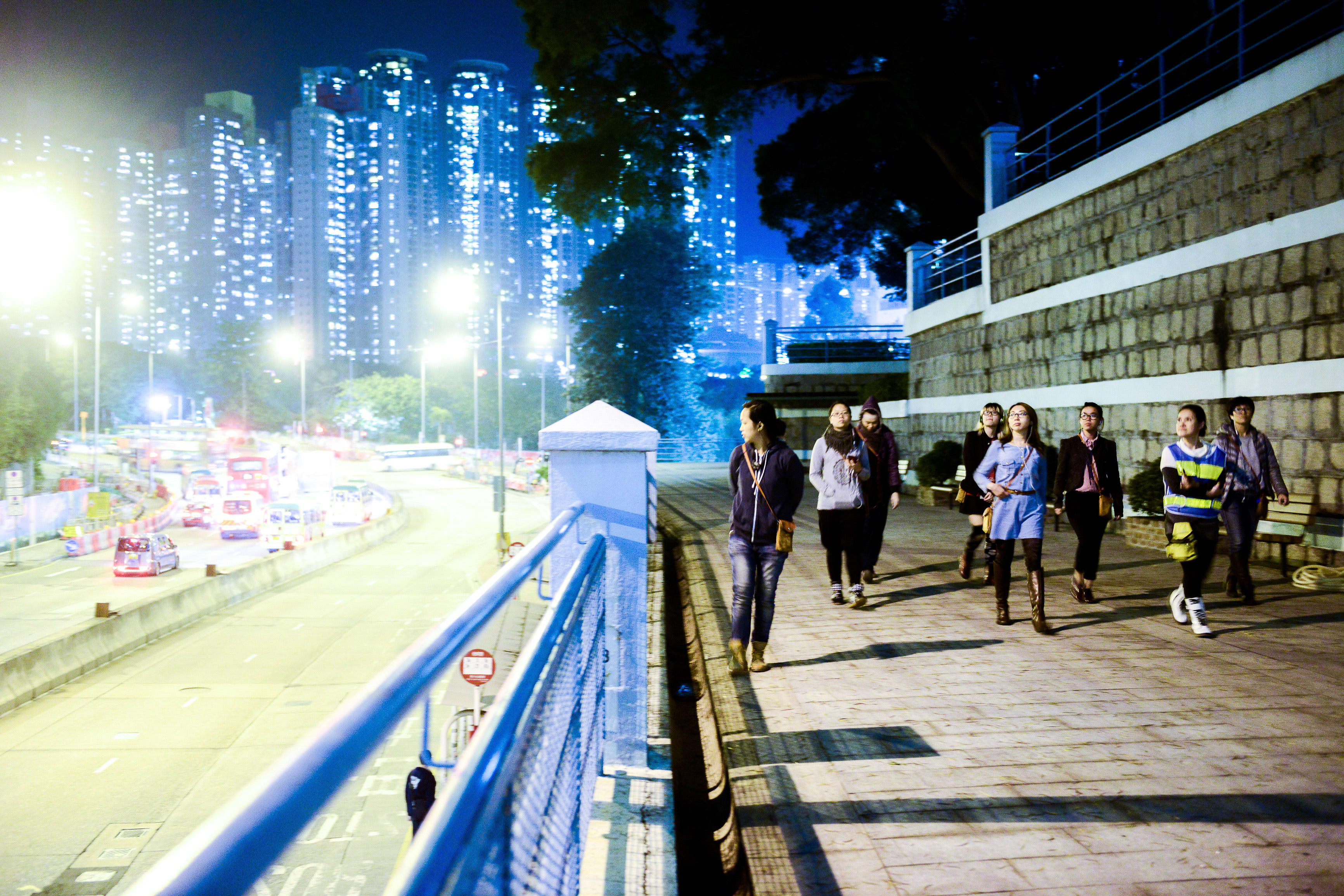 在這張極具氛圍感的夜景照片中，一群演員正走在天台製作當代劇場作品《行為淪喪》的排練場景中。背景是閃爍著燈光的香港摩天大樓，凸顯出劇作對於城市疏離感與人際連結的深刻探索。鏡頭捕捉了演員們行走時的戲劇張力，展現出獨特的現場演出質感。 《行為淪喪》