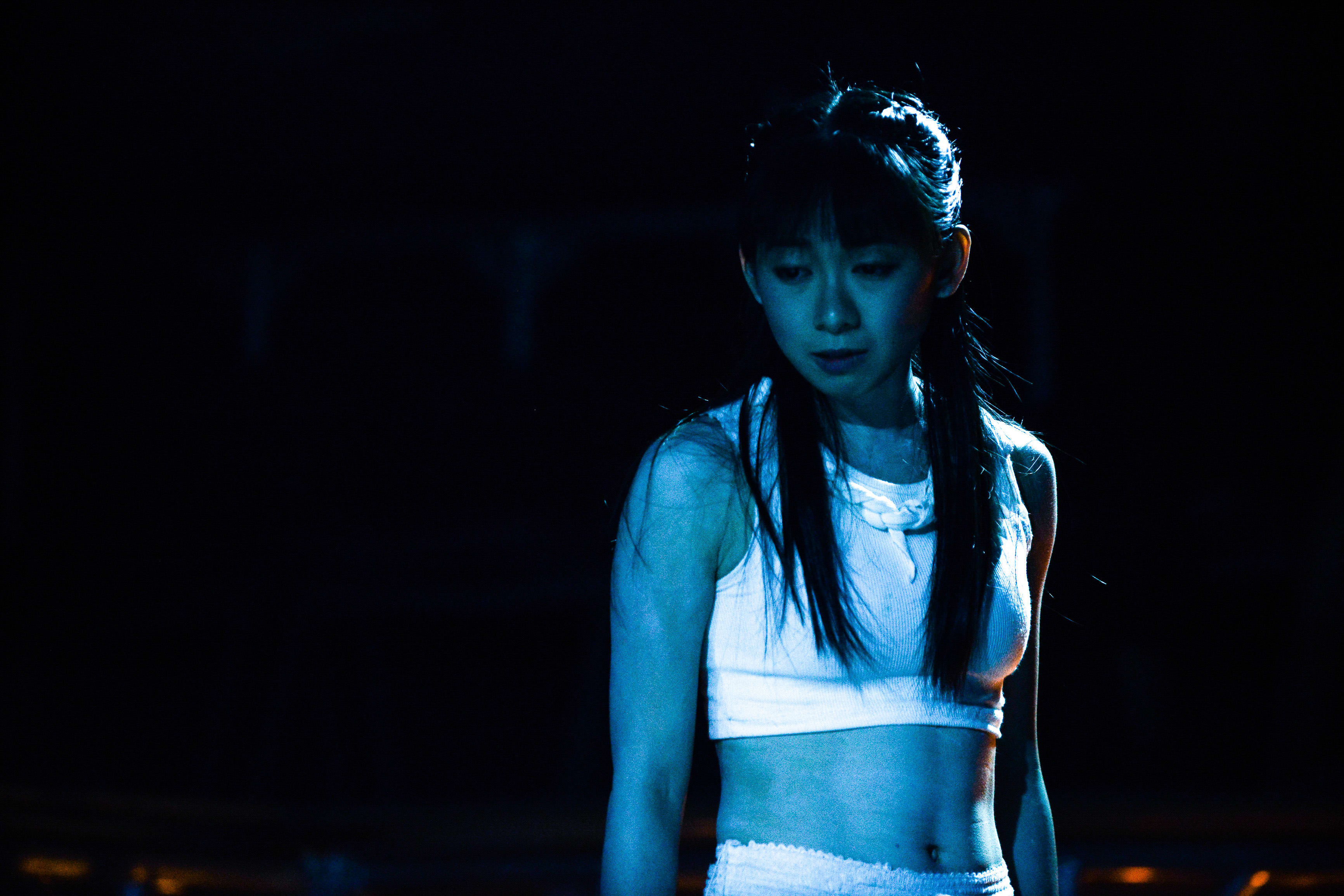 葉嘉茵於天台製作（Rooftop Productions）當代劇場作品《行為淪喪》（The Beautiful Ones）中的演出劇照。在強烈藍色舞台燈光的映照下，葉嘉茵身穿白色短版上衣，神情凝重而內斂，展現出劇場表演中極具張力的情緒表達，體現了香港現代劇場獨有的藝術氛圍。《行為淪喪》。