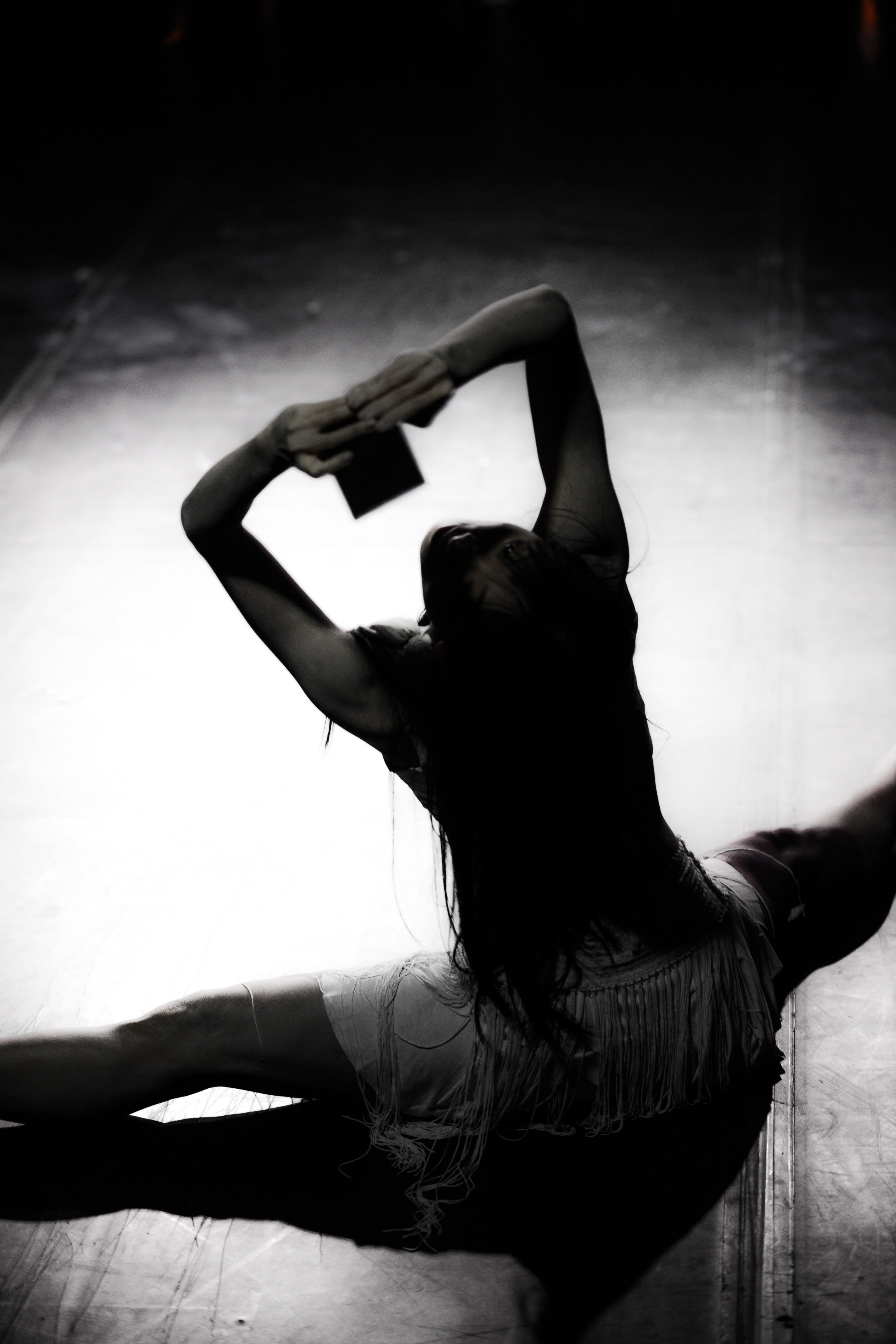 In a dramatic shot from Rooftop Productions' contemporary theatre piece 'The Beautiful Ones' (《行為淪喪》), performer Yip Ka-yan is captured mid-performance in a striking split. Lit by a sharp, high-contrast spotlight against a darkened stage, she extends her arms above her head to form a geometric shape, her body language radiating intense, raw emotion typical of Hong Kong experimental performance art. "The Beautiful Ones"