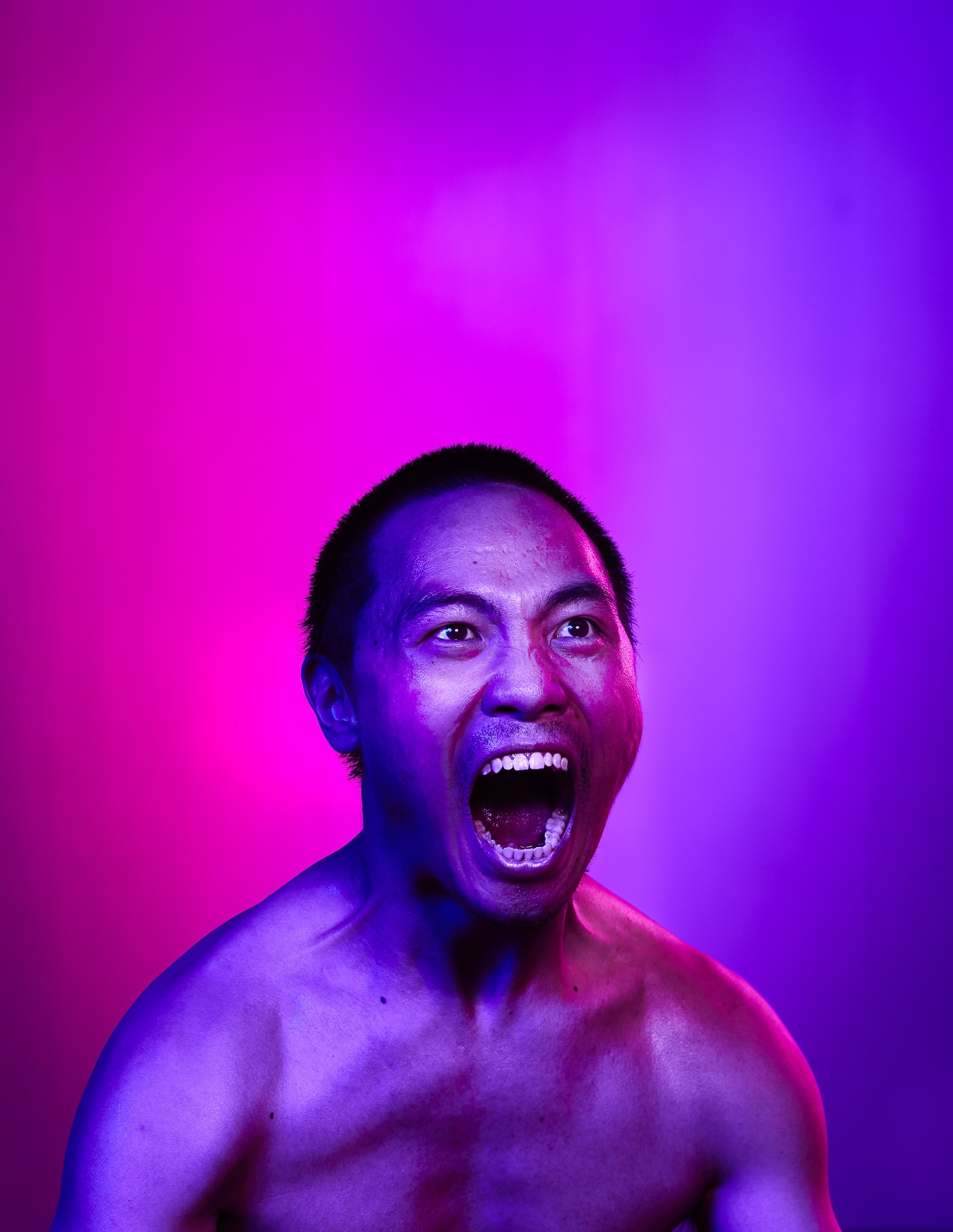 這是香港當代劇團天台製作（Rooftop Productions）舞台劇《復仇變奏曲》（The Furies Variations）的宣傳劇照。演員岑宗達在鏡頭前張大嘴巴，展現出極具張力且深刻的情感爆發，呈現了當代劇場演出中常見的強烈戲劇能量。畫面運用了高對比度的粉紅色與紫色燈光，營造出強烈的舞台效果與視覺衝擊力。岑宗達為《復仇變奏曲》的宣傳照片。