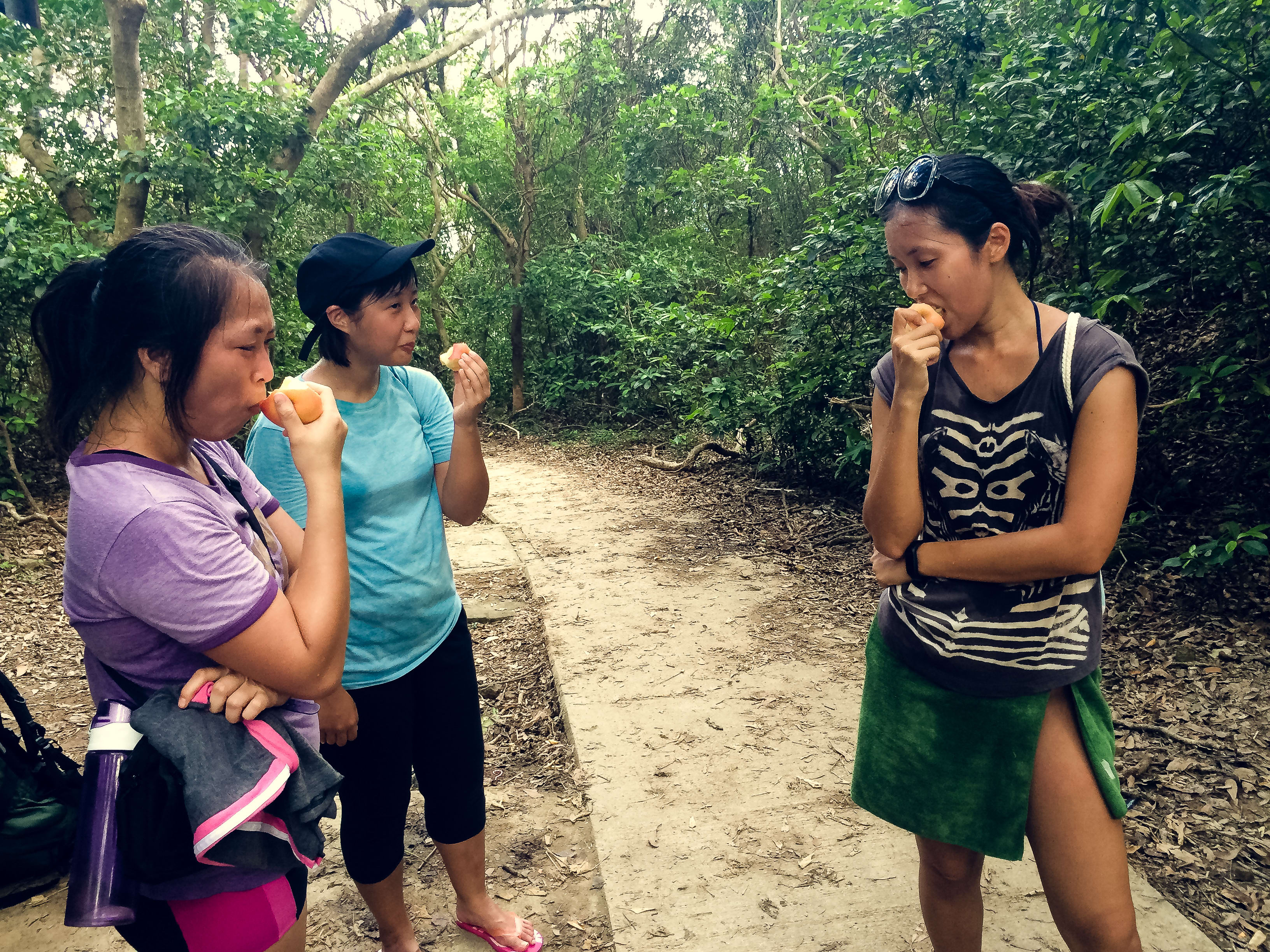 三位參與者於西貢郊野公園進行「當劇場走進大自然2017」(Theatre in Nature 2017) 的形體劇場訓練營，趁著徒步健行期間在茂密的樹林小徑中享用零食。畫面中包括演員梁皓貽，展現了天台製作 (Rooftop Productions) 獨特的環境劇場及在地創作特色。正如營隊成員所言：「離開城市的煩囂．．． 2017」