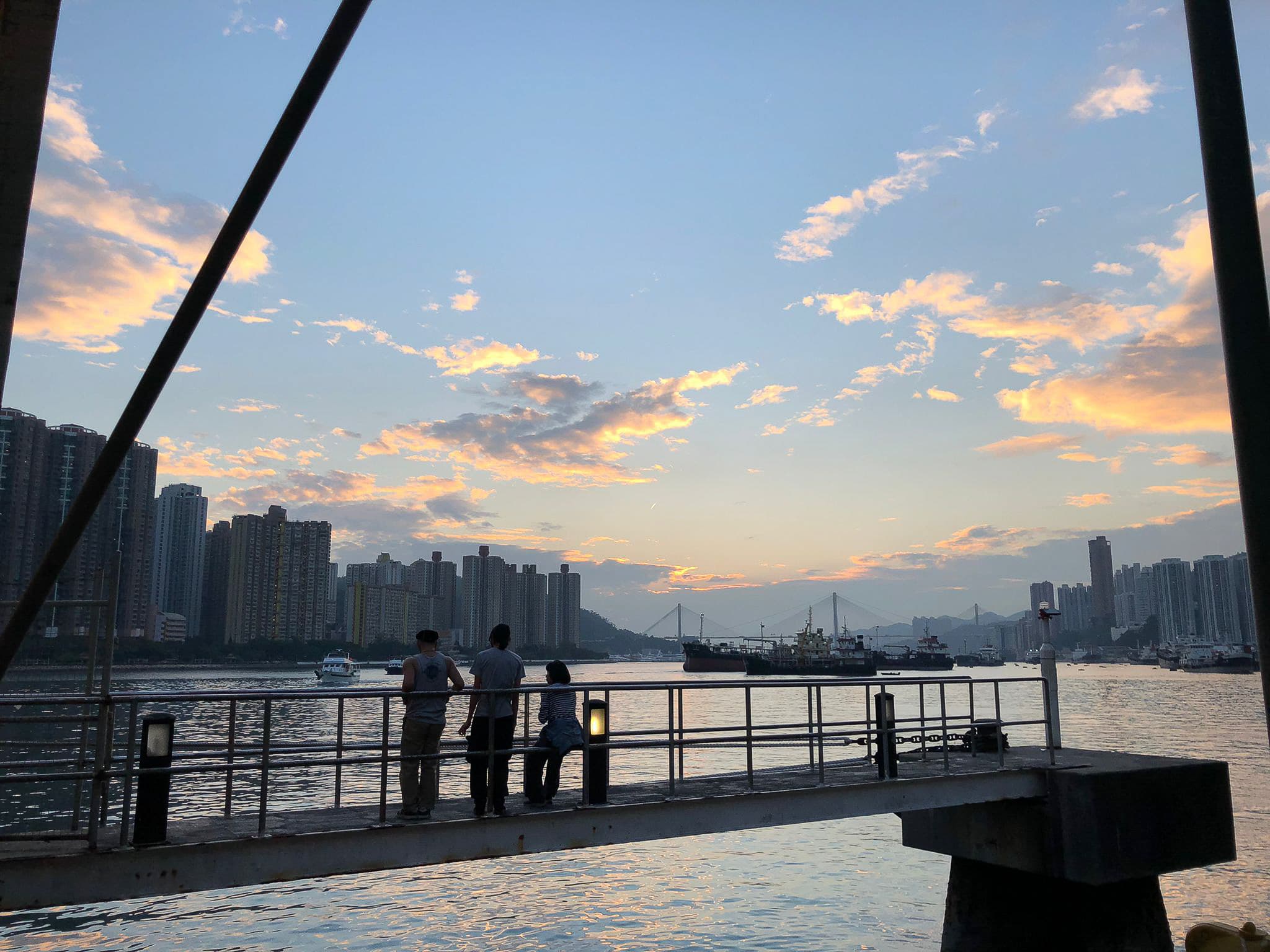 天台製作的演員莫嫣、蘇樂鍵及 Jerry Ip 佇立於碼頭，眺望夕陽下的香港維港，為當代劇場演出《舞照跳》作演出前沉澱。演員在晚霞映照下的剪影，勾勒出演出中對藝術與城市的深刻反思。其中一名演員望向海平線，輕聲說道：「希望」。