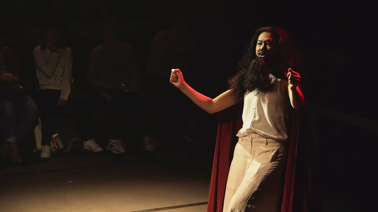 《復仇變奏曲》完整演出視頻的寬銀幕縮圖，呈現了一位表演者在昏暗的劇場舞台上演出的場景。演員身穿白色上衣、淺色長褲並披著戲劇性的深紅色斗篷，臉上留著濃密的鬍鬚，在聚光燈下展現充滿張力的動作。背景幽暗，突顯了這部香港當代劇場作品的強烈舞台氛圍。