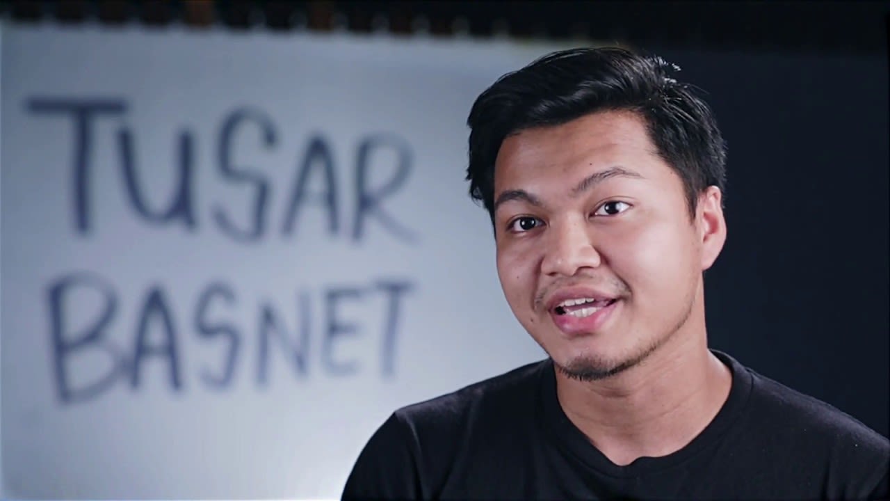 這是一張演員 Tusar Basnet 的特寫鏡頭，背景明亮，牆上寫著他名字的黑色手寫字樣。這張照片捕捉了他真實的表情，展現了香港當代劇場演出中自然、細膩的表演風格。