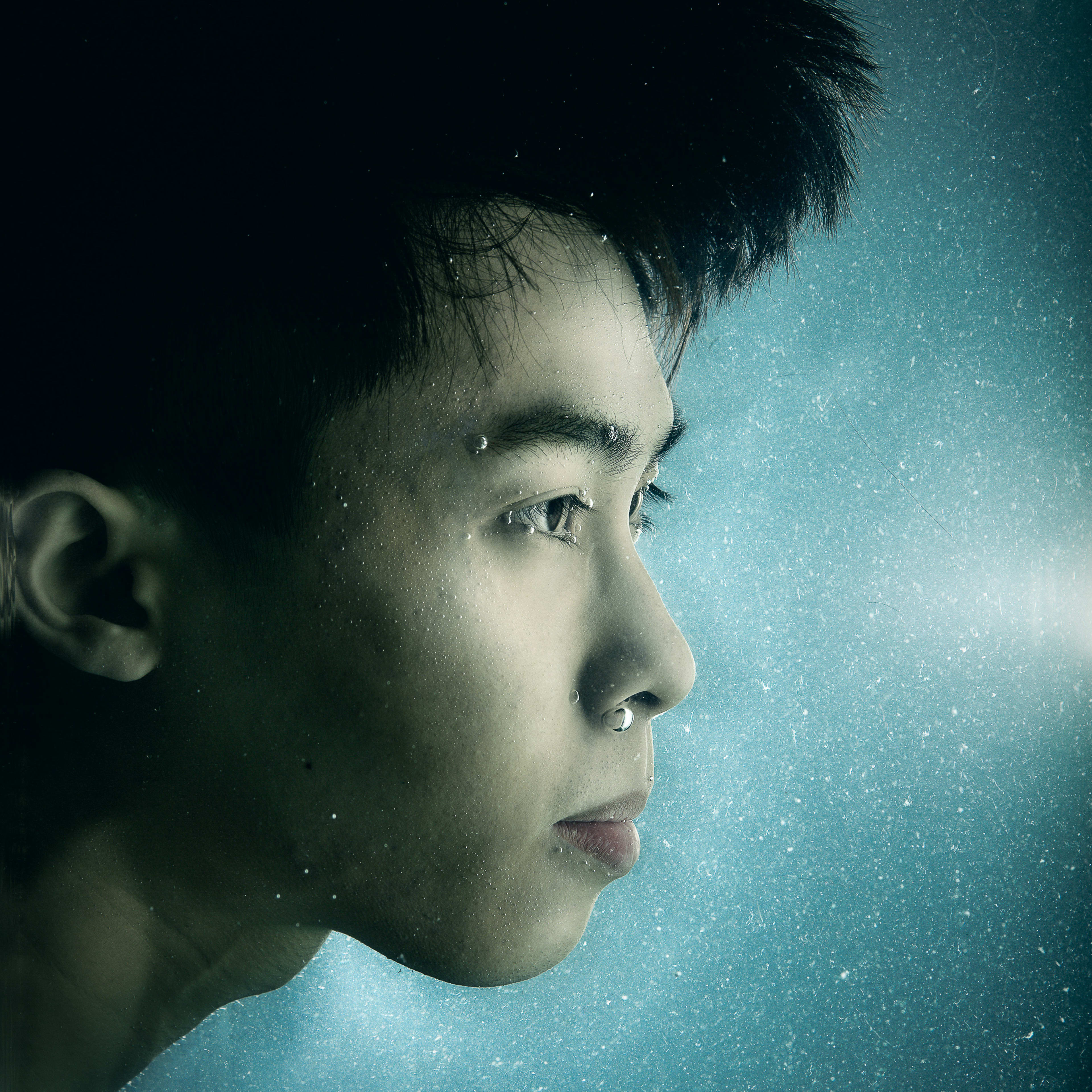 A dramatic close-up of Hong Kong actor Chiu Chin Hei, shot underwater for the Rooftop Productions contemporary theatre piece 'Lost Shoreline'. The blue, ethereal lighting highlights air bubbles clinging to his skin and face, evoking a sense of isolation and environmental loss. This striking portrait captures the poignant aesthetic of the production. 'Lost Shoreline'