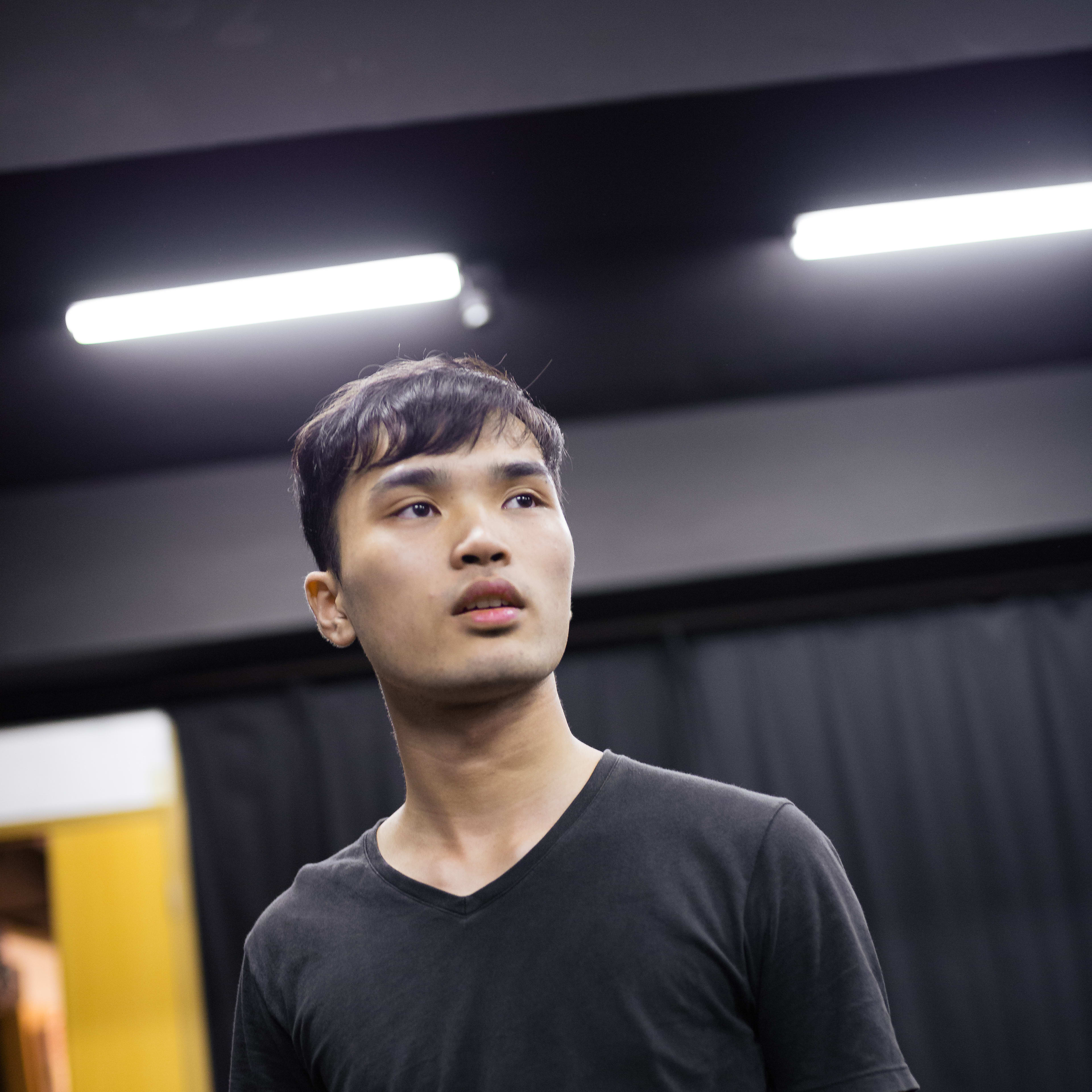 一名年輕男演員在香港「身心合一」表演訓練工作坊中的特寫鏡頭。他身穿黑色 V 領上衣，神情專注地望向鏡頭外，展現了當代劇場肢體訓練的張力與專注感。Psychophysical actor training workshops in Hong Kong, 2016.