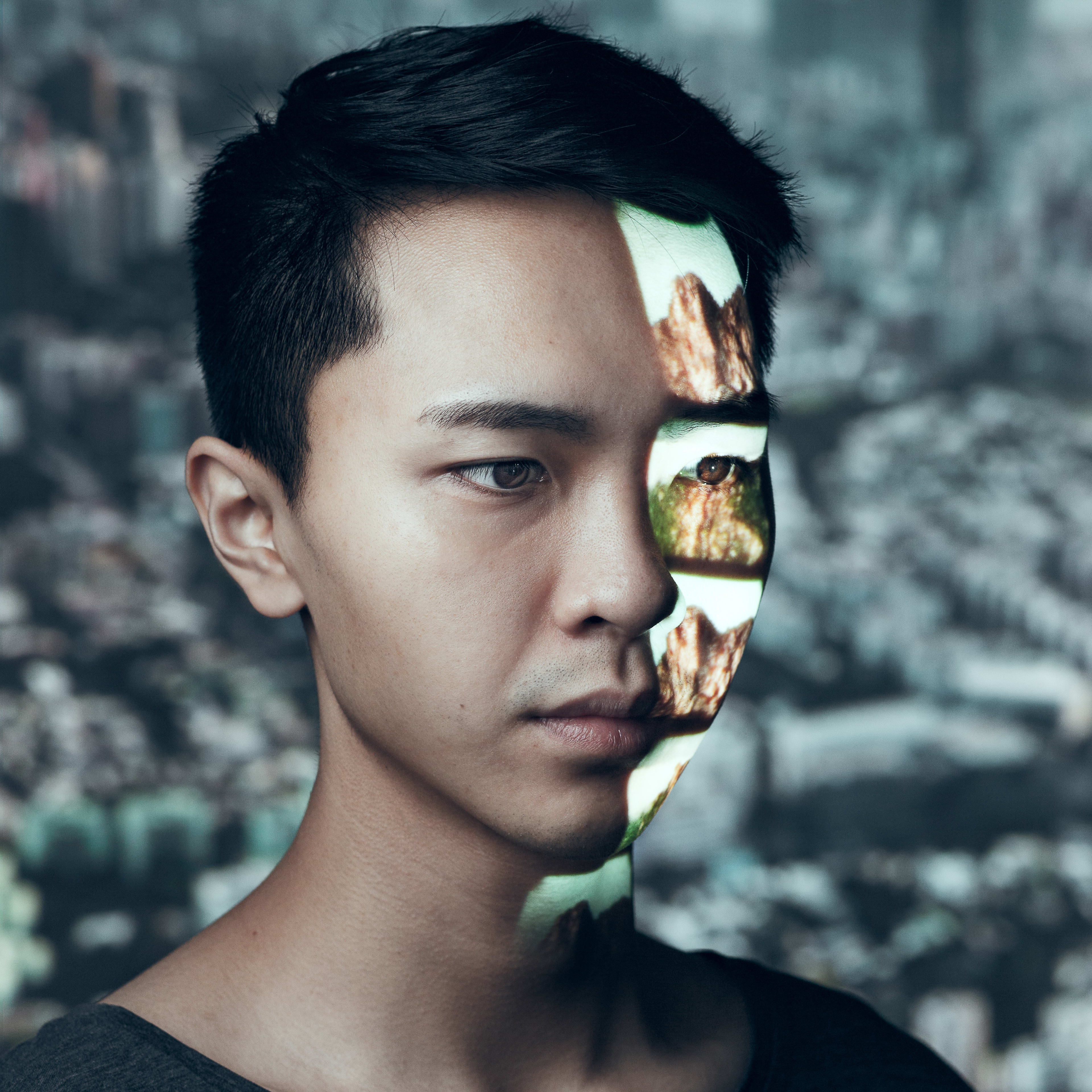 天台製作（Rooftop Productions）當代劇場作品《山下的證詞》（Testimony）之宣傳劇照，由演員吳景隆出演。影像捕捉了演員沉思的表情，其面部左側投影著崎嶇山脈的視覺影像，與背景中虛化的香港城市景觀形成強烈對比，呈現出人與土地、城市記憶交織的劇場意象。《山下的證詞》