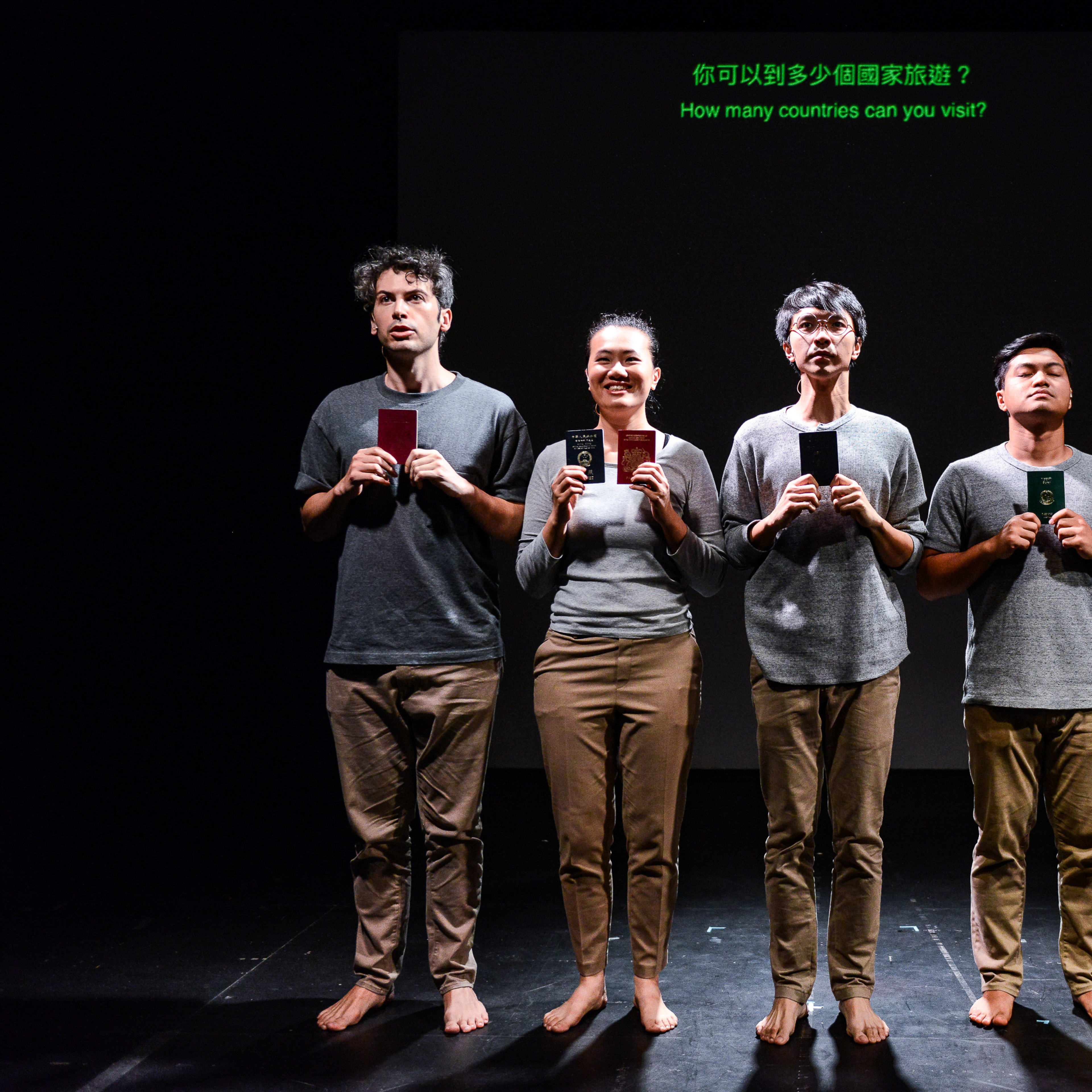 在天台製作的當代劇場作品《山下的證詞》中，五位演員站在昏暗的極簡風格舞台上，背景為純黑。每位演員手持一本護照，象徵著不同程度的全球通行權。由左至右分別為：艾浩家 (Ivor Houlker)、李婉晶 (Michelle Li)、吳景隆 (Ng King Lung)、巫加沙 (Mohammad Kashif Ali) 及 Basnet Tusar。他們頭頂的屏幕顯示著問題：「你可以到多少個國家旅遊？」。這部強而有力的舞台劇探討了身份、特權與國籍等議題。演員們神情肅穆地演繹著這句台詞：「根據你的護照可免簽証到訪的地方總數排好。」