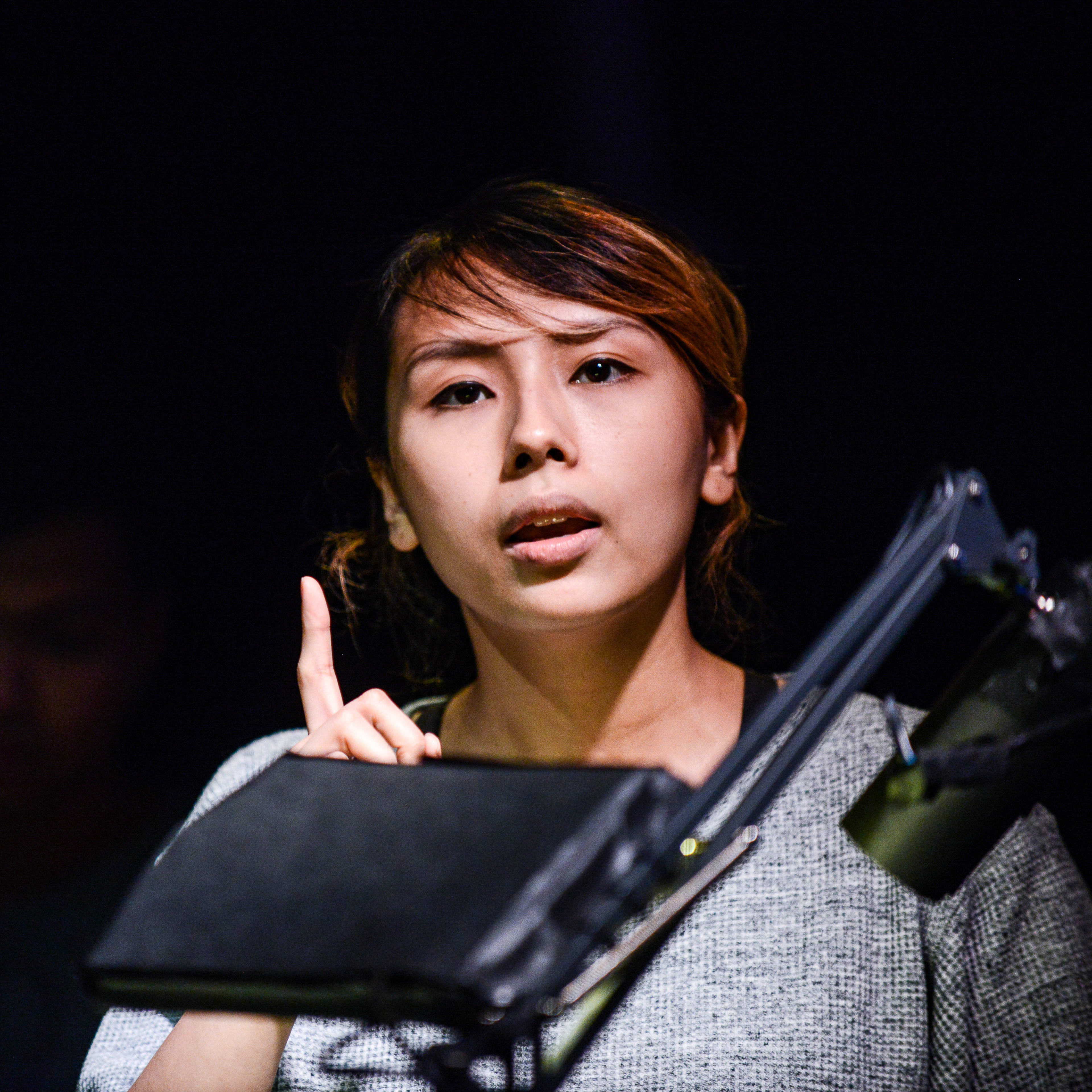 李里莎（Arisa Yasaratne）正在為天台製作的當代香港劇場作品《山下的證詞》（Testimony）進行排練，舞台燈光在黑暗的背景下聚焦於她身上。她舉起食指，神情專注地演繹著劇中片段，並說道：「近來又一部電影是關於全球最有名的巴斯人。」