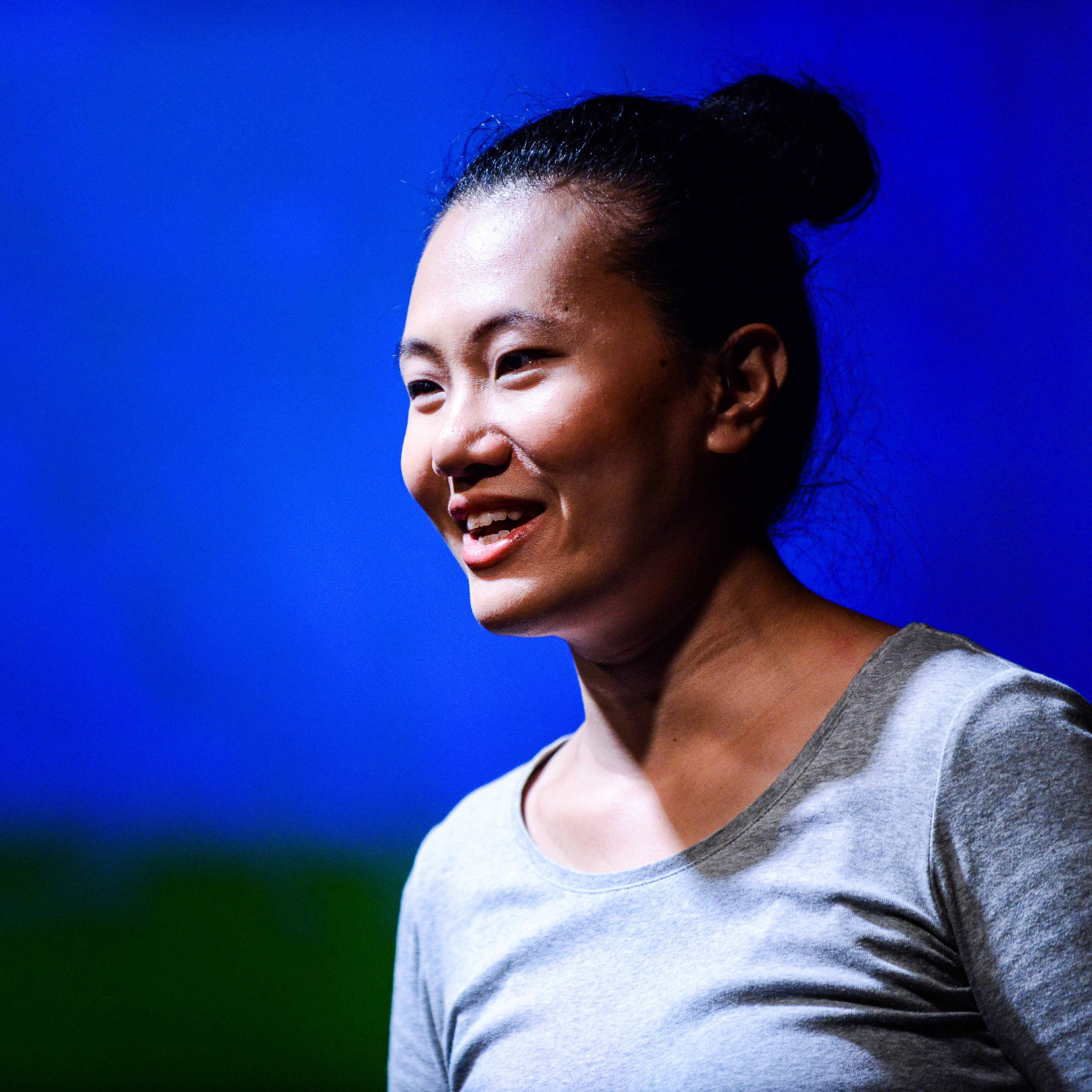 演員李婉晶於天台製作（Rooftop Productions）的當代劇場作品《山下的證詞》（Testimony）中的演出劇照。在強烈的藍色舞台燈光映襯下，她身穿簡約灰色上衣，髮髻高盤，神情專注而充滿張力，展現了劇作獨特的情感深度。《山下的證詞》