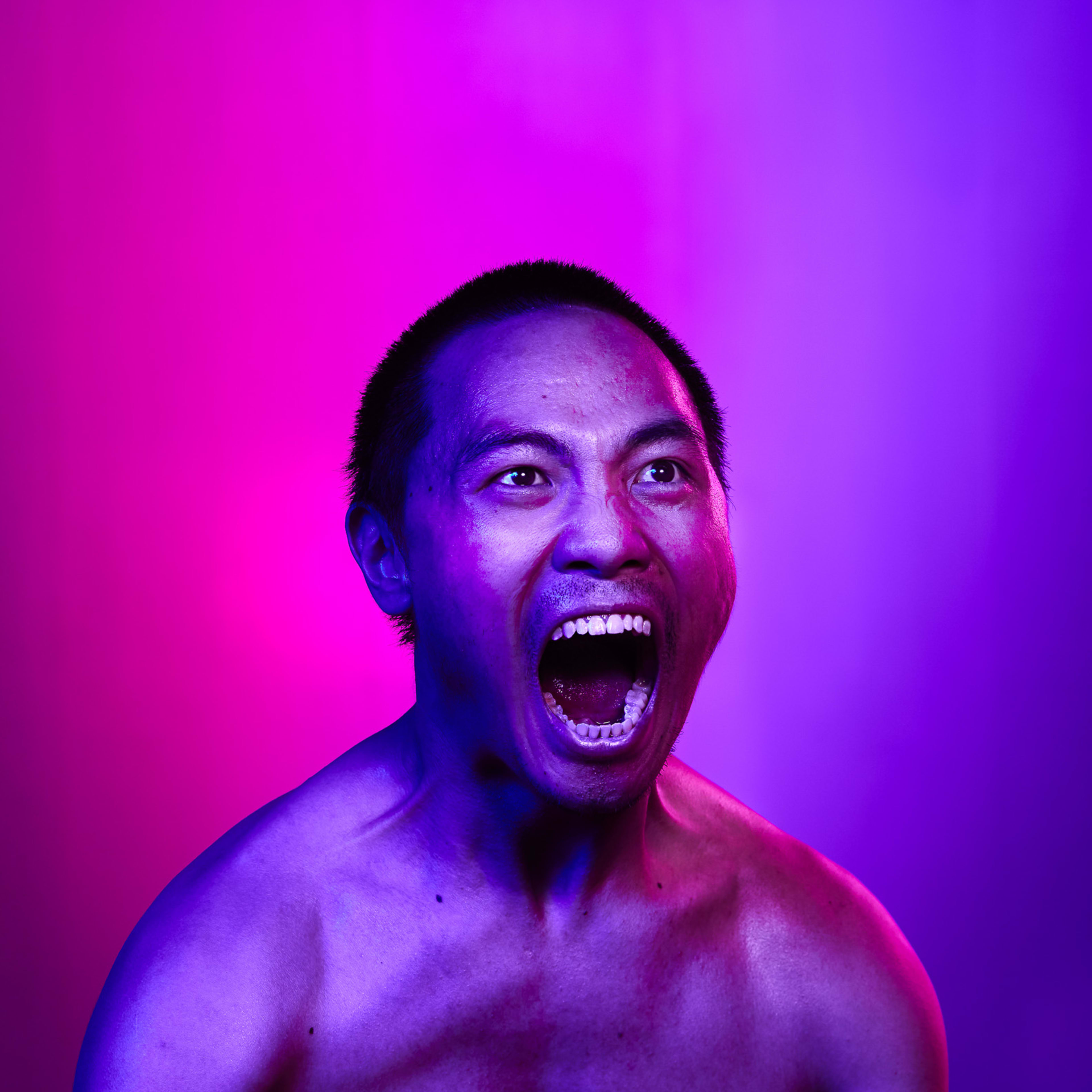 這是香港當代劇團天台製作（Rooftop Productions）舞台劇《復仇變奏曲》（The Furies Variations）的宣傳劇照。演員岑宗達在鏡頭前張大嘴巴，展現出極具張力且深刻的情感爆發，呈現了當代劇場演出中常見的強烈戲劇能量。畫面運用了高對比度的粉紅色與紫色燈光，營造出強烈的舞台效果與視覺衝擊力。岑宗達為《復仇變奏曲》的宣傳照片。