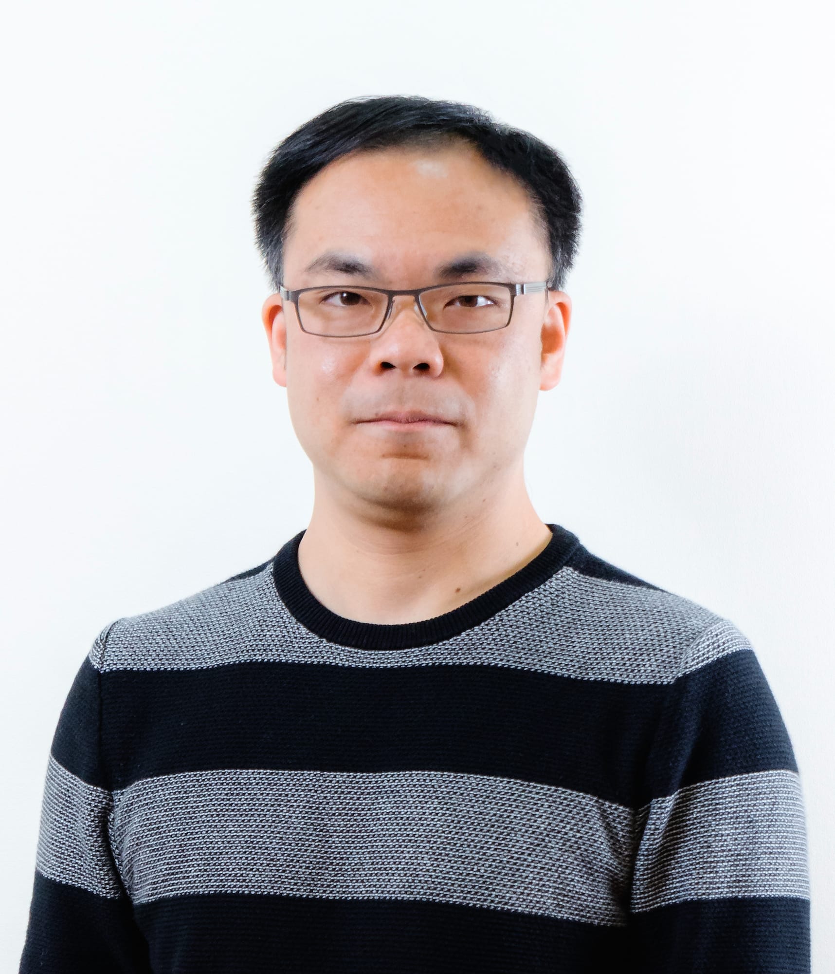 A professional headshot of Hong Kong theatre practitioner William Chan (陳瑋鑫), known for his work with Rooftop Productions (天台製作). He is captured against a clean, white background, wearing a casual black and grey striped sweater, looking directly at the camera with a neutral expression and glasses.