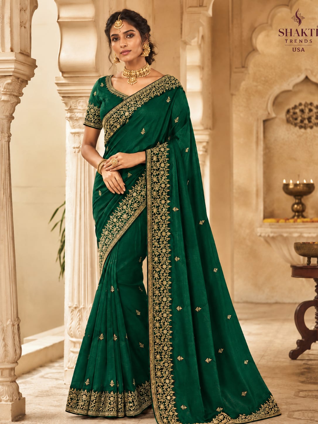 South Asian woman wearing an emerald green traditional saree with gold embroidery and matching jewelry in a palace-style setting.