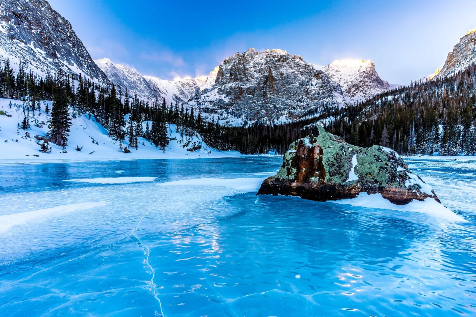 Blue Ice at The Loch — Rocky Mountain National Park, Colorado. Wind-polished ice glowing electric blue around a snow-capped boulder at The Loch in Rocky…