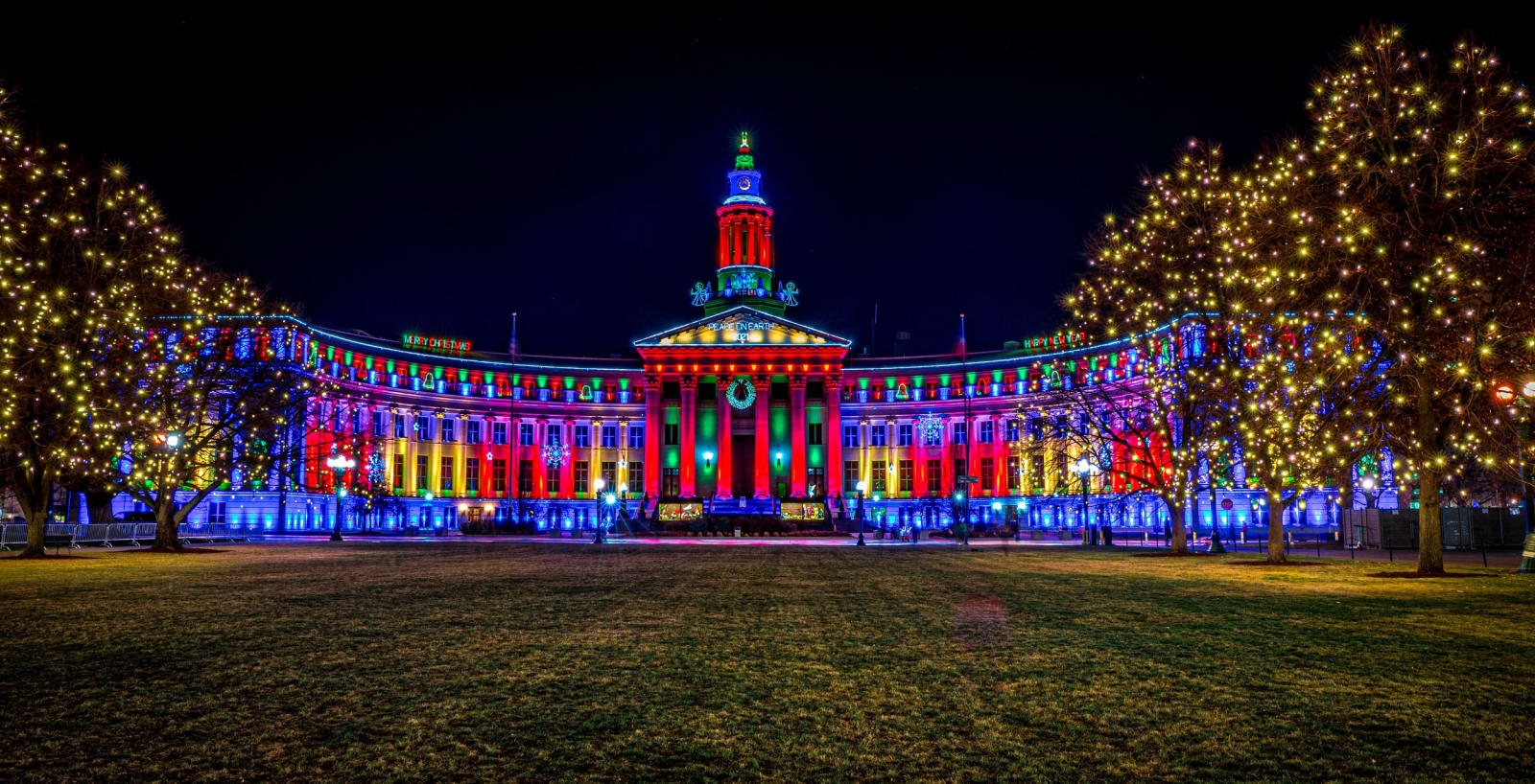 The Building in Full Dress — Denver, Colorado. The Denver City and County Building in full holiday dress, every column lit in red, blue, and gold with the…