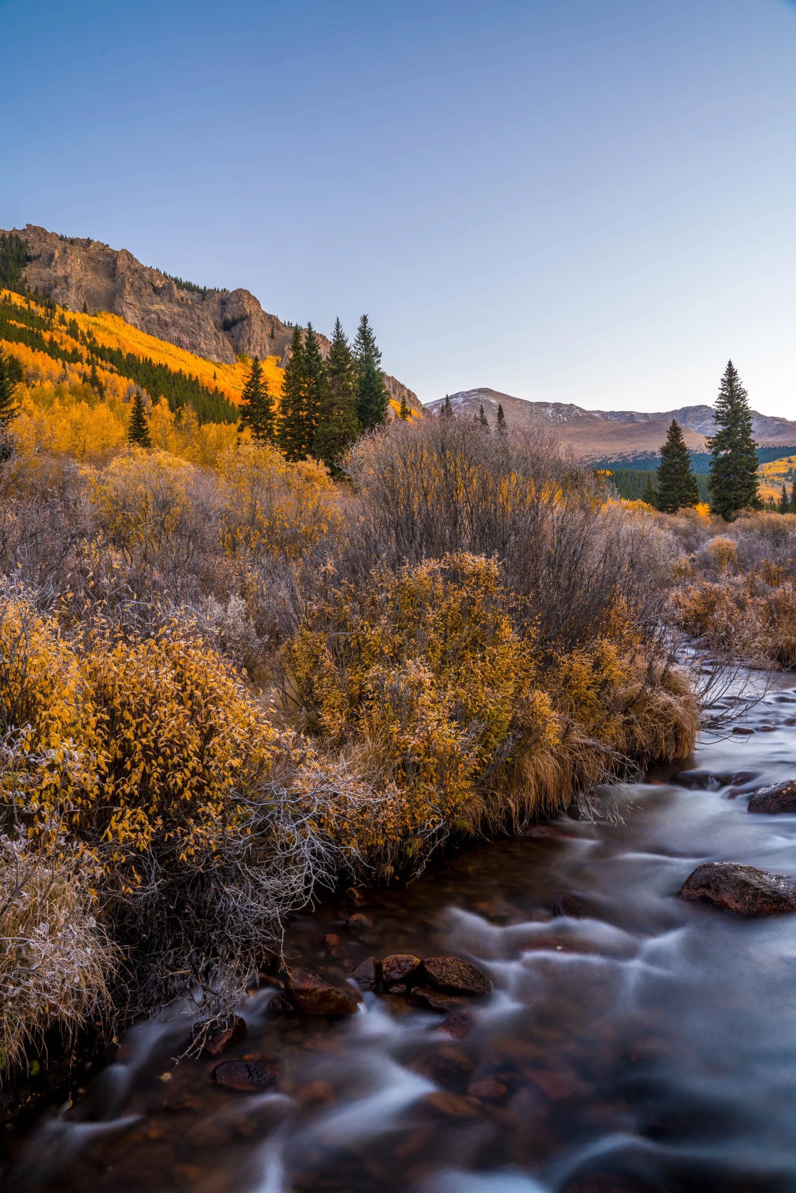 Two Seasons Before Breakfast — Abyss Lake Trail, Colorado. First sun lighting the aspen ridge while the creek below stays in cold shade, frost hanging on…