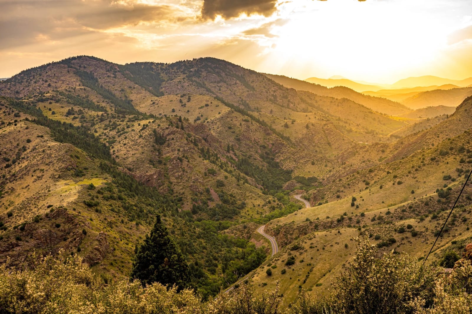 Canyon Road in Sun Flare — Clear creek canyon. Sun flare pouring over the ridges while a canyon road threads the bottom of a golden Colorado foothills valley.