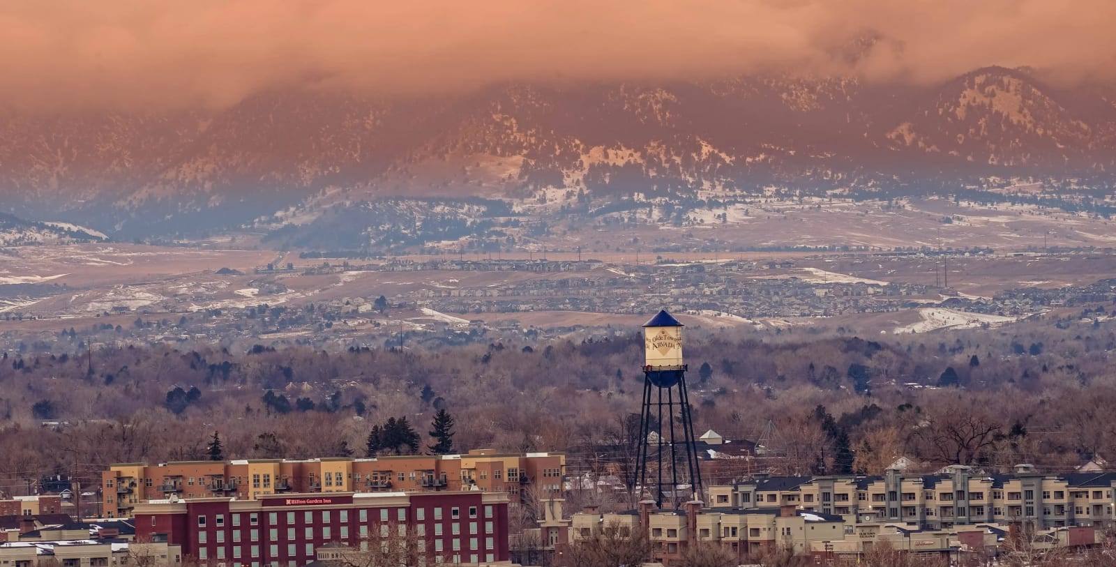 Water Tower Against the Front Range — Arvada, Colorado. The Olde Town Arvada water tower stacked tight against the snow-dusted foothills, with a long lens…