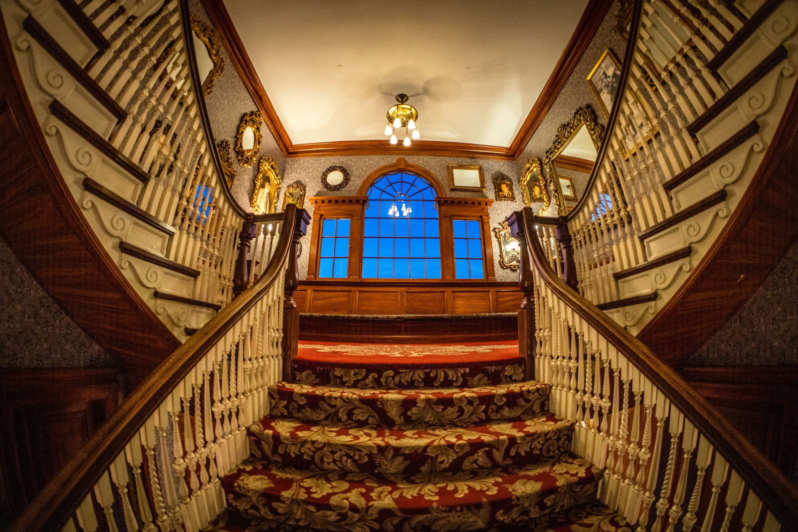 Up Toward the Landing — Estes Park, Colorado. Looking up the Stanley Hotel staircase toward the arched window and chandelier, red carpet climbing into warm…