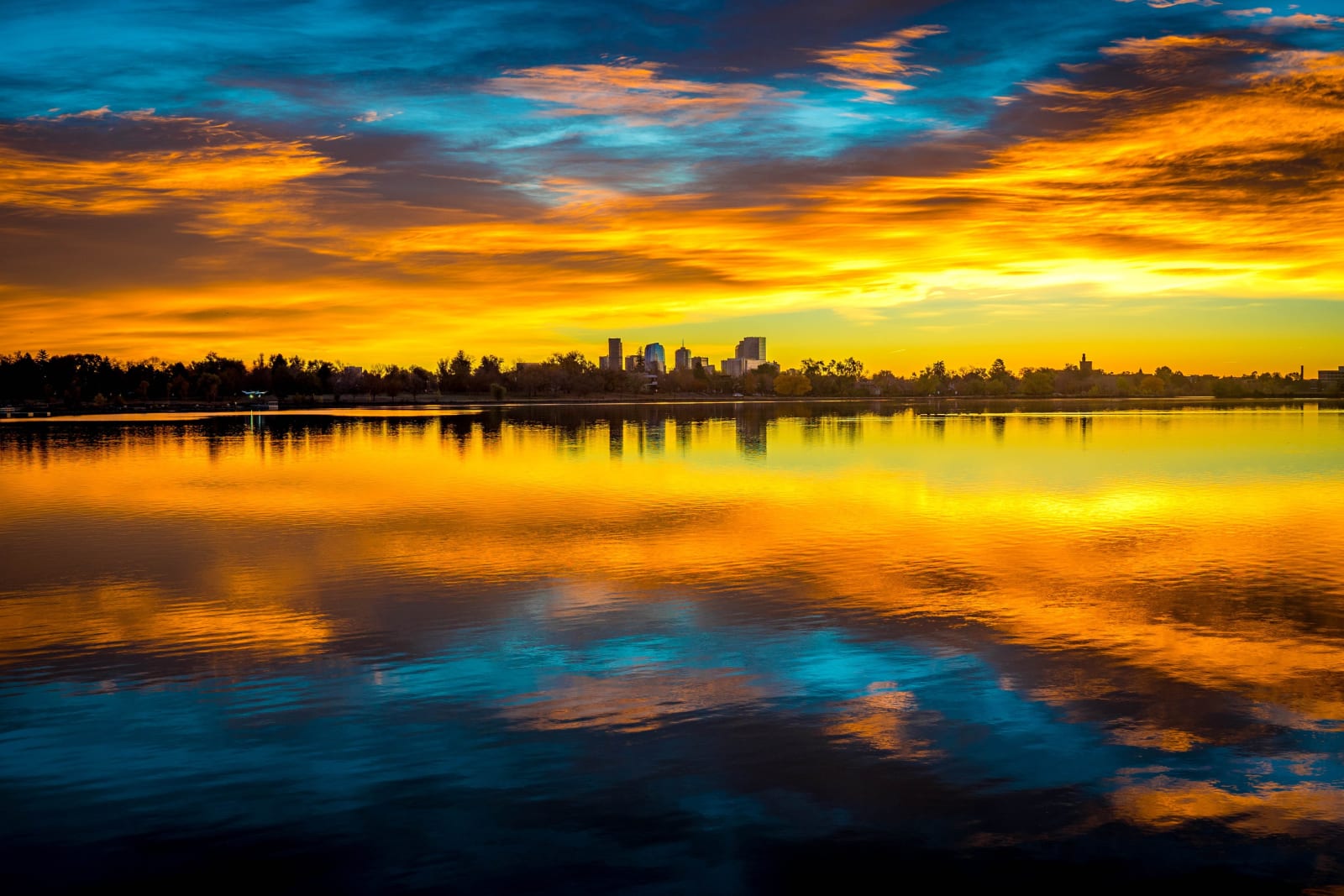 Orange Band Over Sloan's Lake — Sloan's Lake, Denver. A wide view across Sloan's Lake in Denver, Colorado, as sunrise lights a band of cloud orange above a…