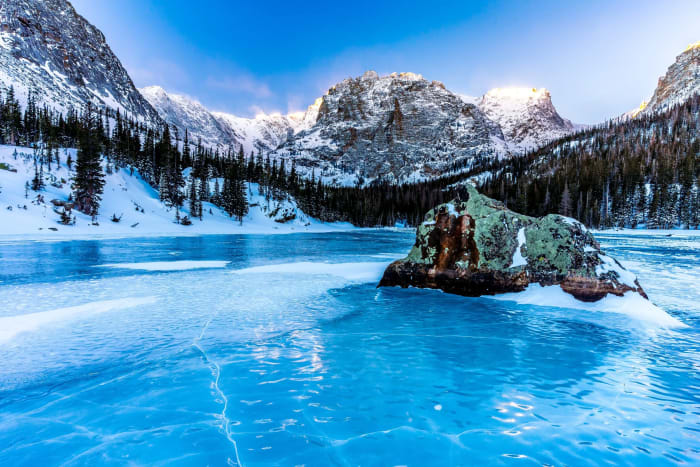 Blue Ice at The Loch — Rocky Mountain National Park, Colorado. Wind-polished ice glowing electric blue around a snow-capped boulder at The Loch in Rocky…