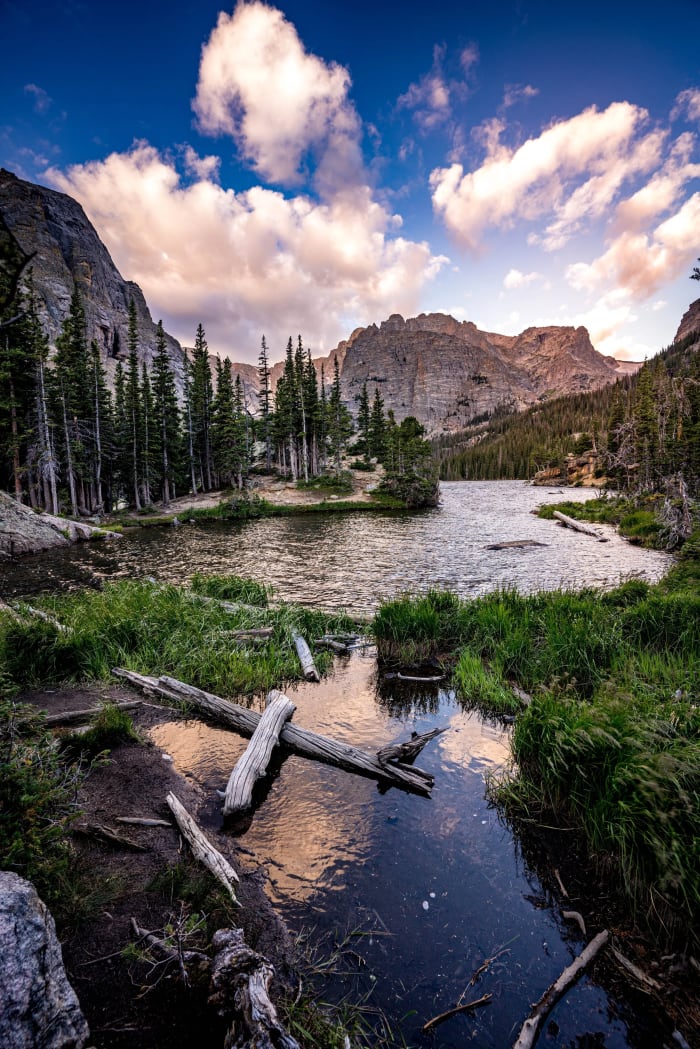 Driftwood at The Loch — Rocky Mountain National Park, Colorado. Driftwood and calm water at The Loch in Rocky Mountain National Park with the clouds above…