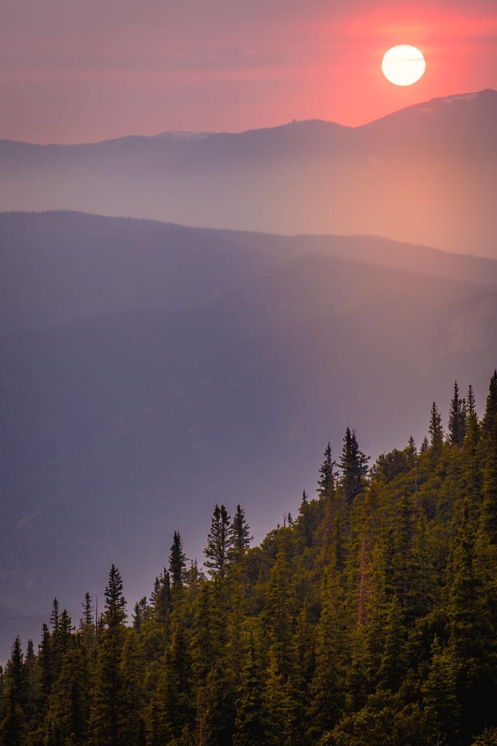 Smoke Season Sunset — Mestaa'ehehe Mountain, Colorado. Wildfire haze turning a Mestaa'Ehehe Mountain sunset into soft lavender and gold, with spruce tops…