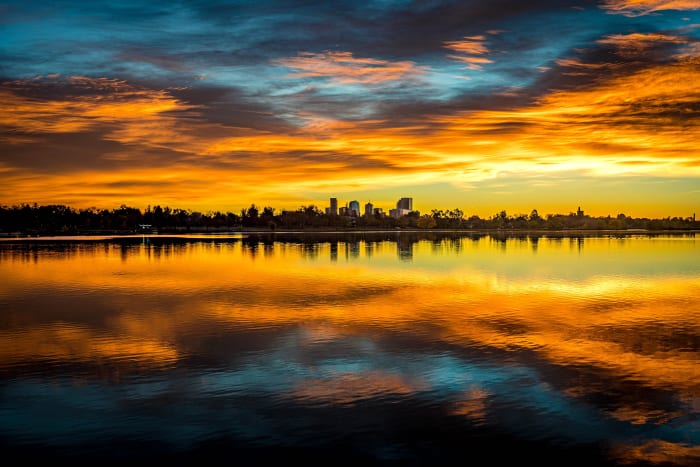 Sloan-rise — Sloan's Lake, Denver. Sunrise over Sloan's Lake in Denver, Colorado, with a wide band of orange cloud above the downtown skyline and the whole…