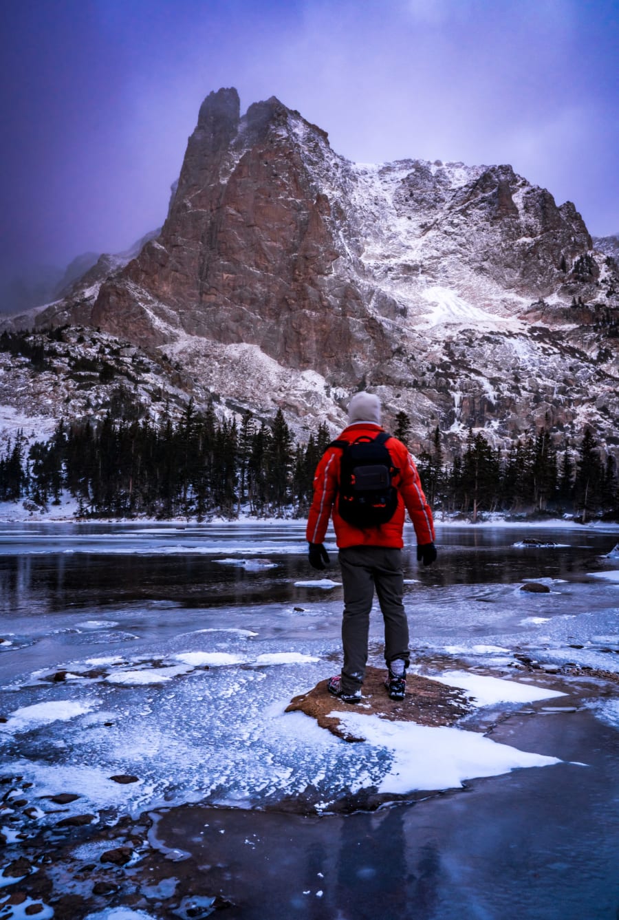 Chris Heaton standing on a frozen alpine lake below a snow-covered peak